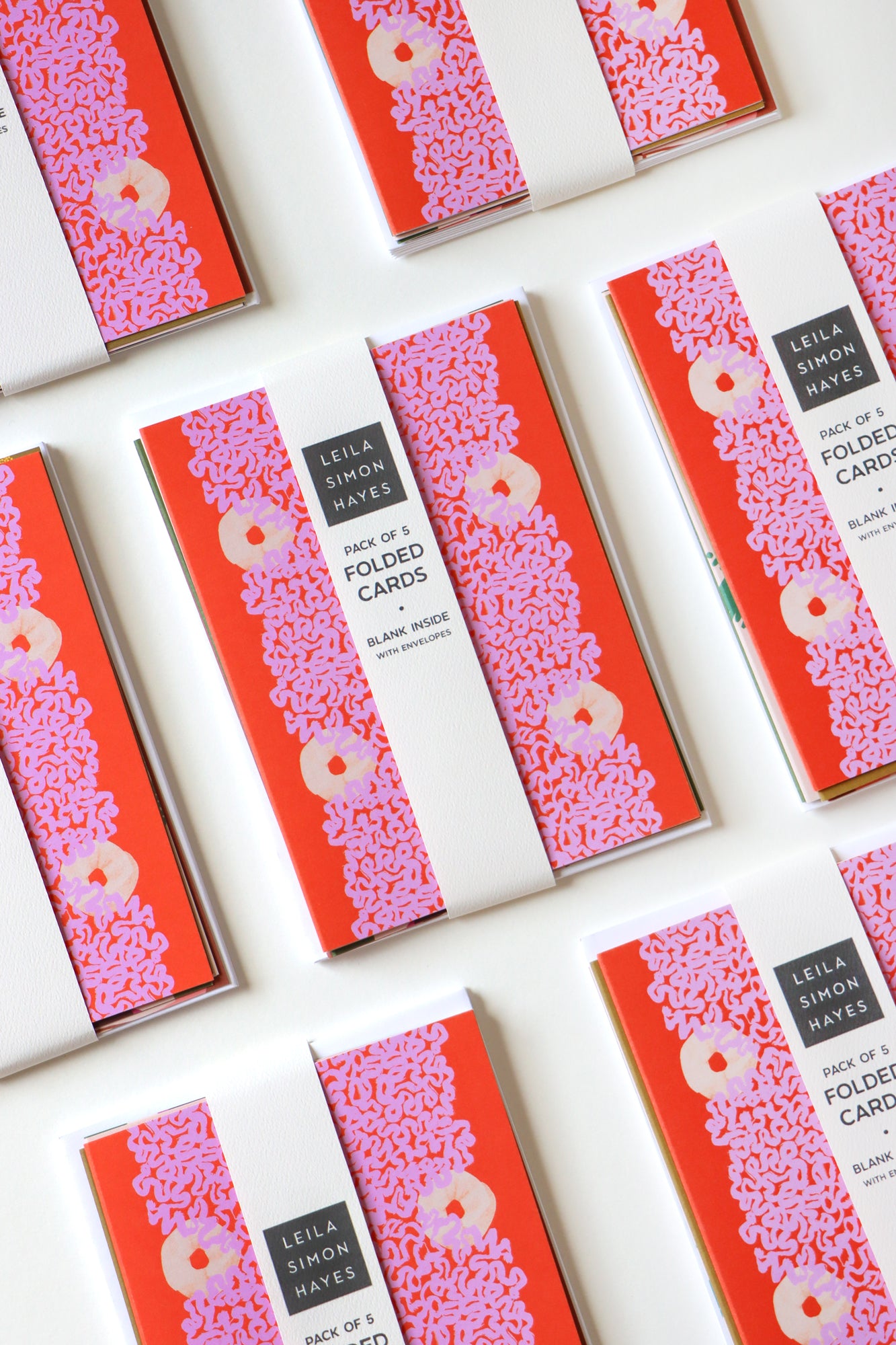 Packaged abstract art cards with red and pink designs on a white background