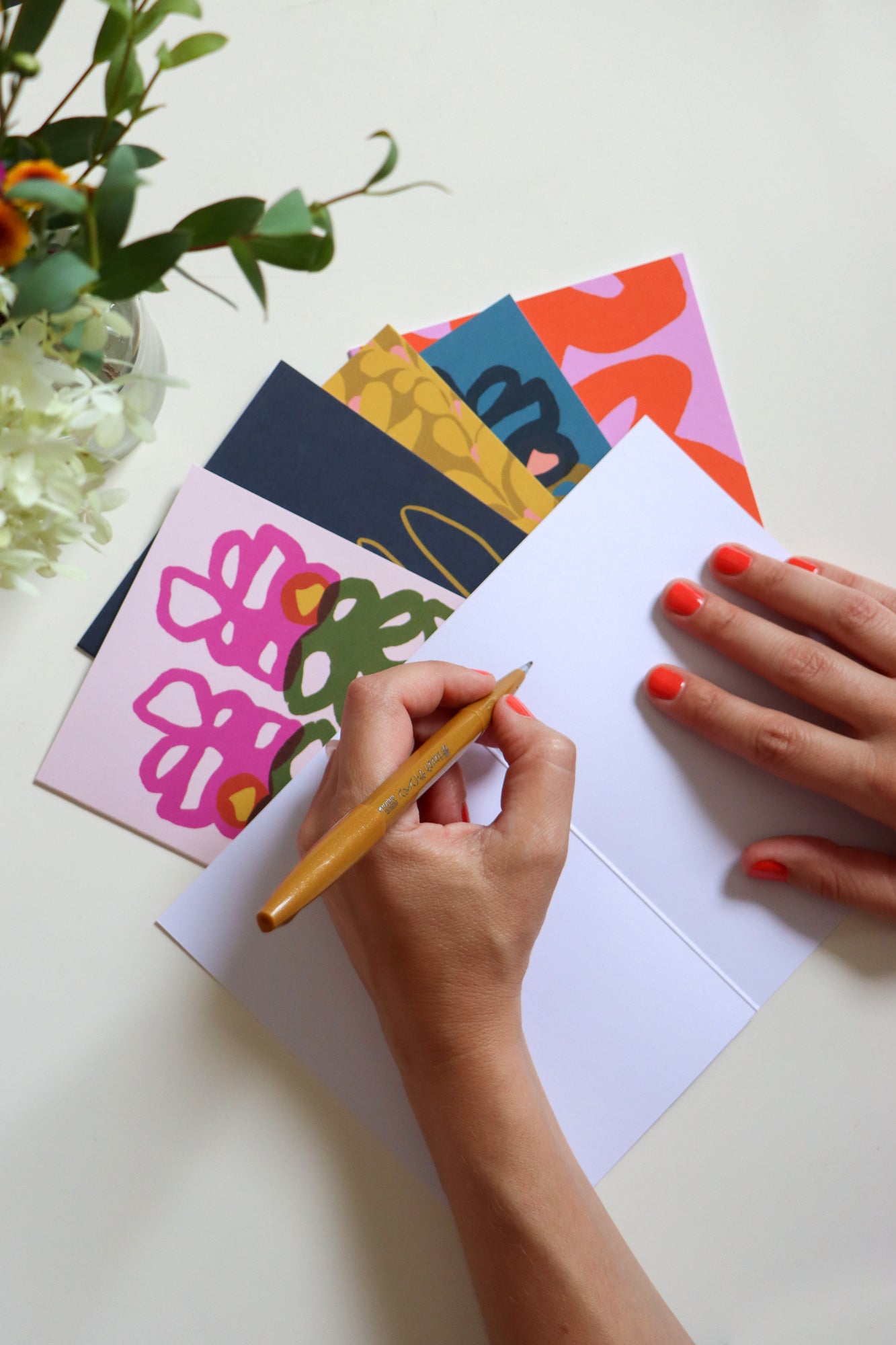 Person writing on a white card with colorful cards and flowers in the background