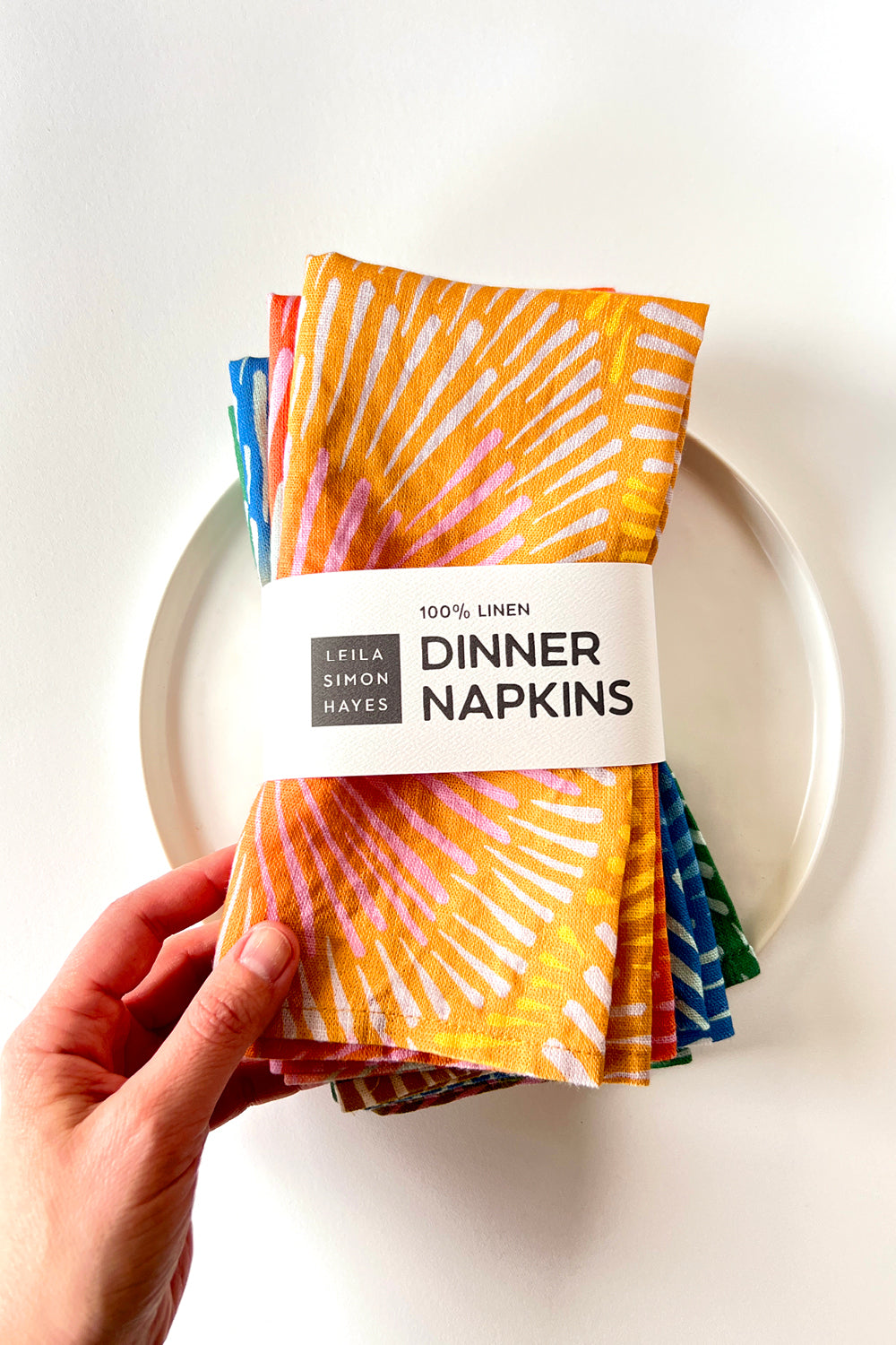 Pack of unique, artful dinner napkins held by a hand with a white background