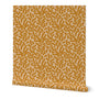 A roll of wallpaper with a hand-painted gold floral, climbing vine pattern on a beige base.
