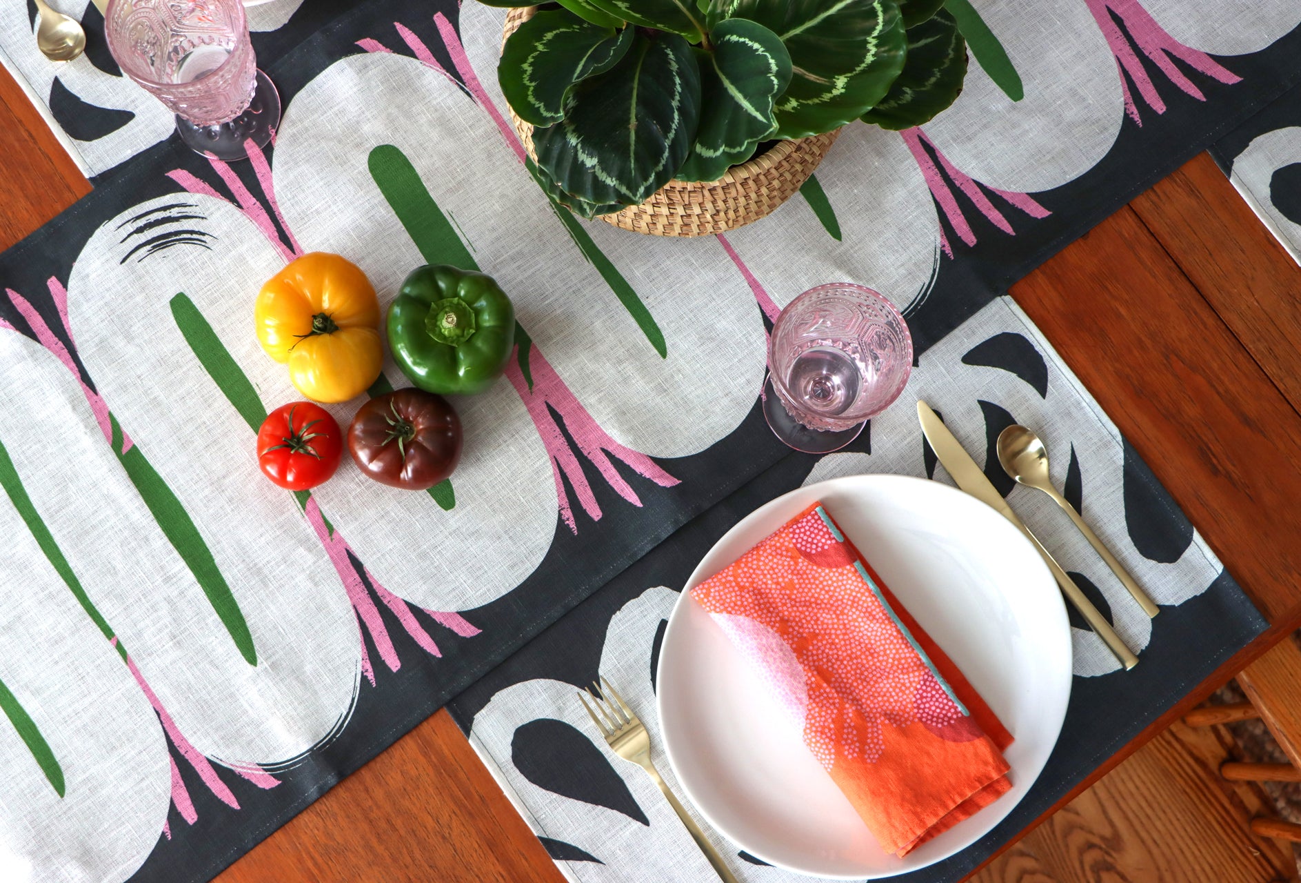 Table setting with colorful placemats, napkins, and table runners, with vegetables and a plant.