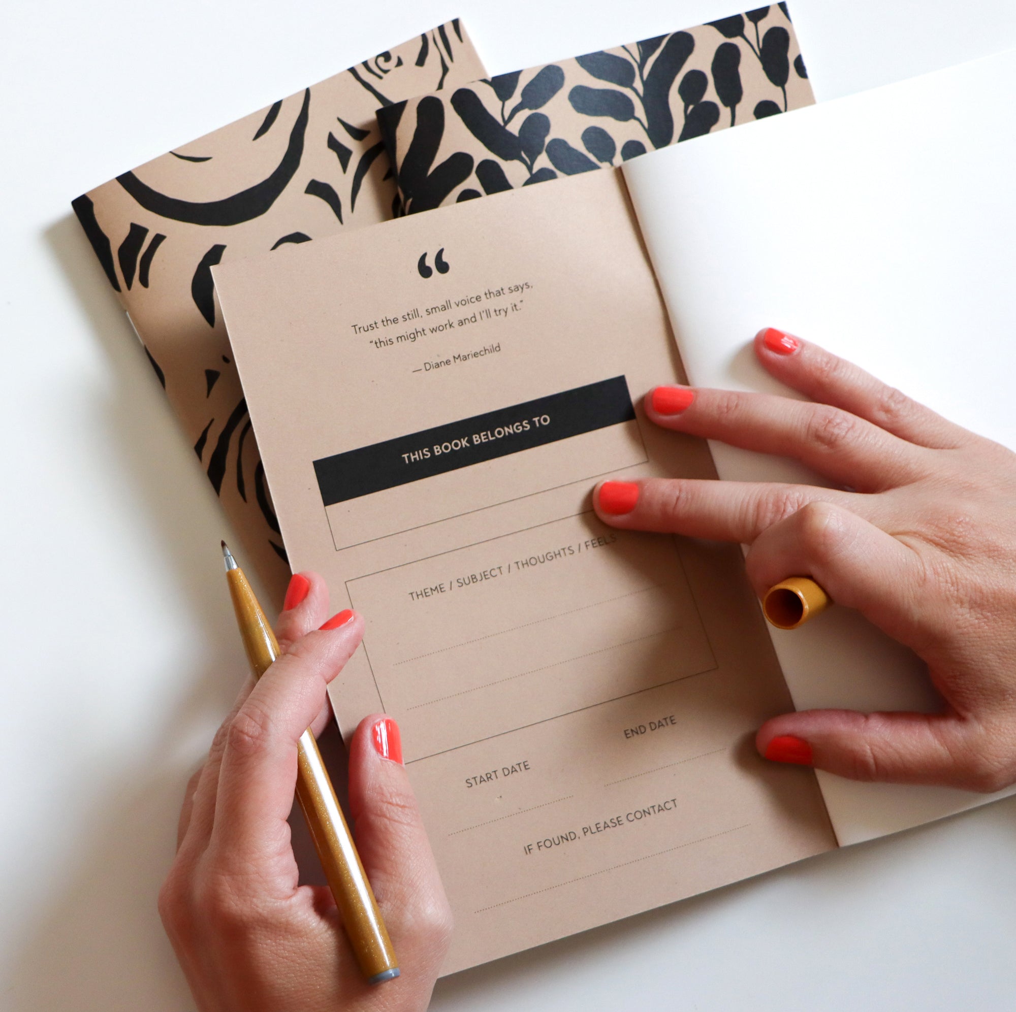 Person opening the inside of a journal with a 'This Book Belongs To' label and a pen, on a white surface.