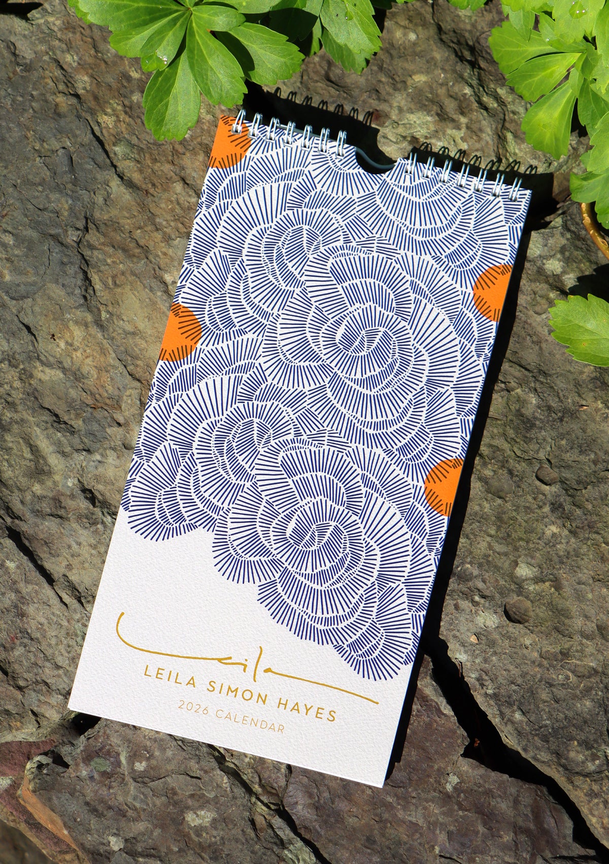 Art calendar with abstract floral design by Leila Simon Hayes on a stone surface with greenery