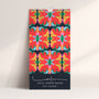 A wall calendar titled '2027 CALENDAR' by Leila Simon Hayes, featuring a bold, symmetrical floral kaleidoscope pattern in coral, pink, yellow, green, and blue on a dark background, leaning against a light beige wall. Designed by artist Leila Simon Hayes.