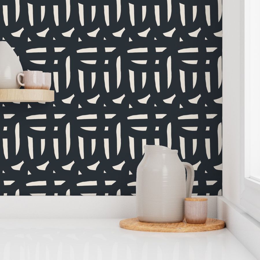 A section of wallpaper with a black on white geometric pattern, featuring hand painted designs, applied to a wall in a home setting with decorative items on top. Designed by artist Leila Simon Hayes.