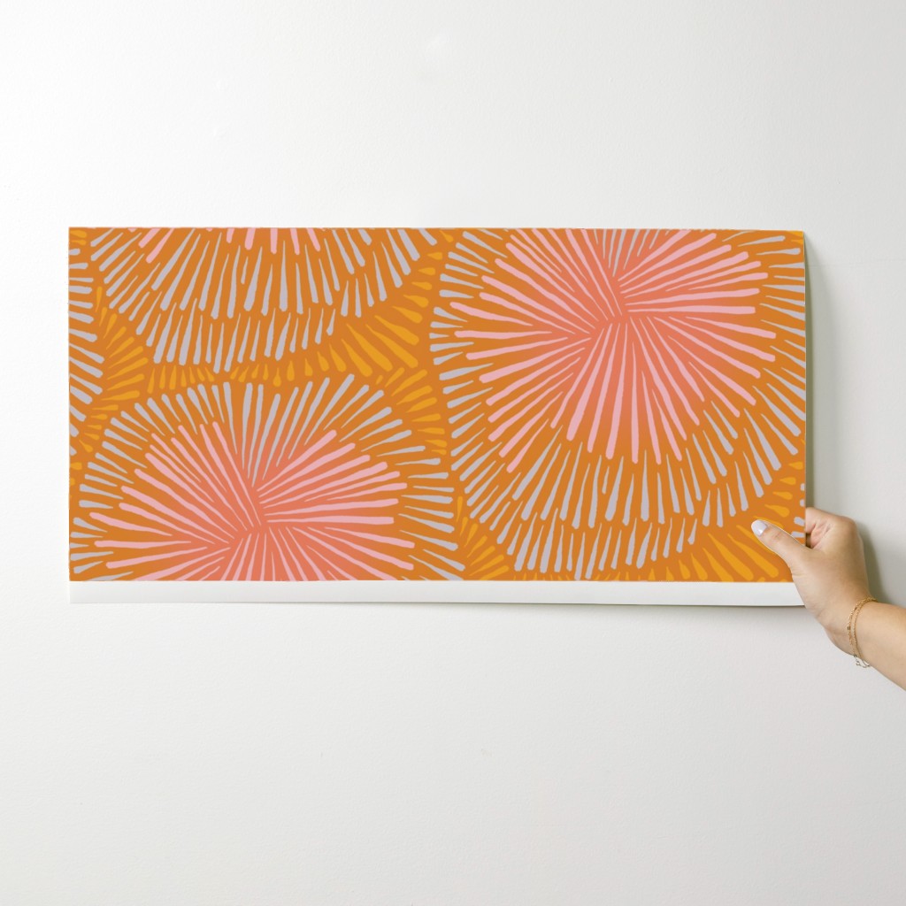 Hand holding a wallpaper swatch with a geometric pattern on a white background. Designed by artist Leila Simon Hayes.