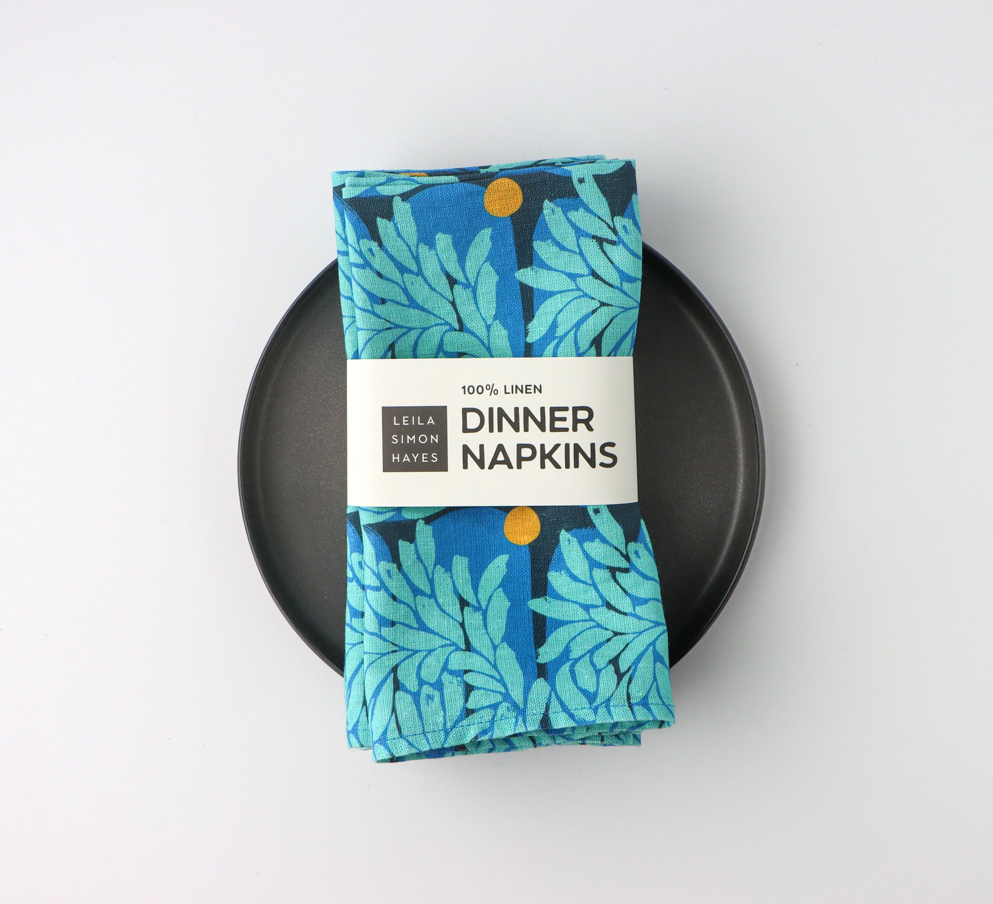 Pack of four,  bright blue floral patterned dinner napkins with a label saying "100% Linen Dinner Napkins", designed by artist Leila Simon Hayes.