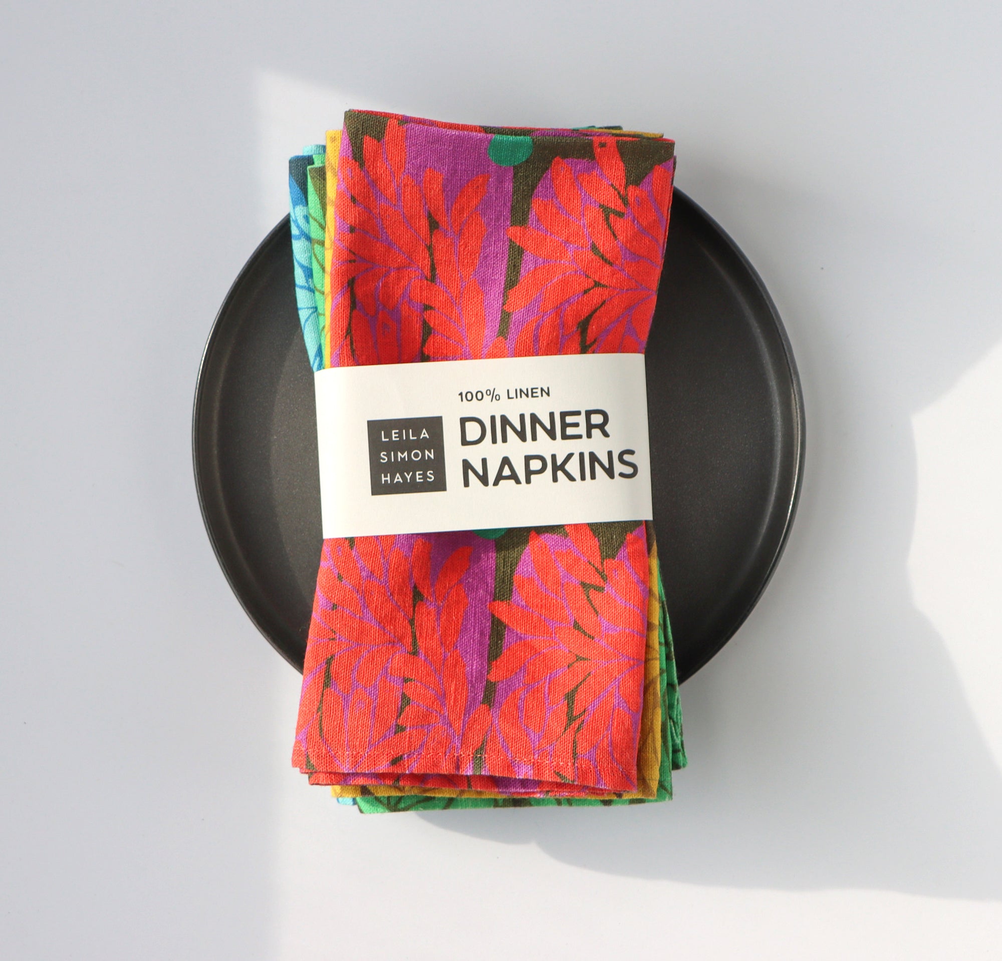 A pack of four colorful, aesthetic dinner napkins with a label saying "100% Linen Dinner Napkins", designed by artist Leila Simon Hayes.