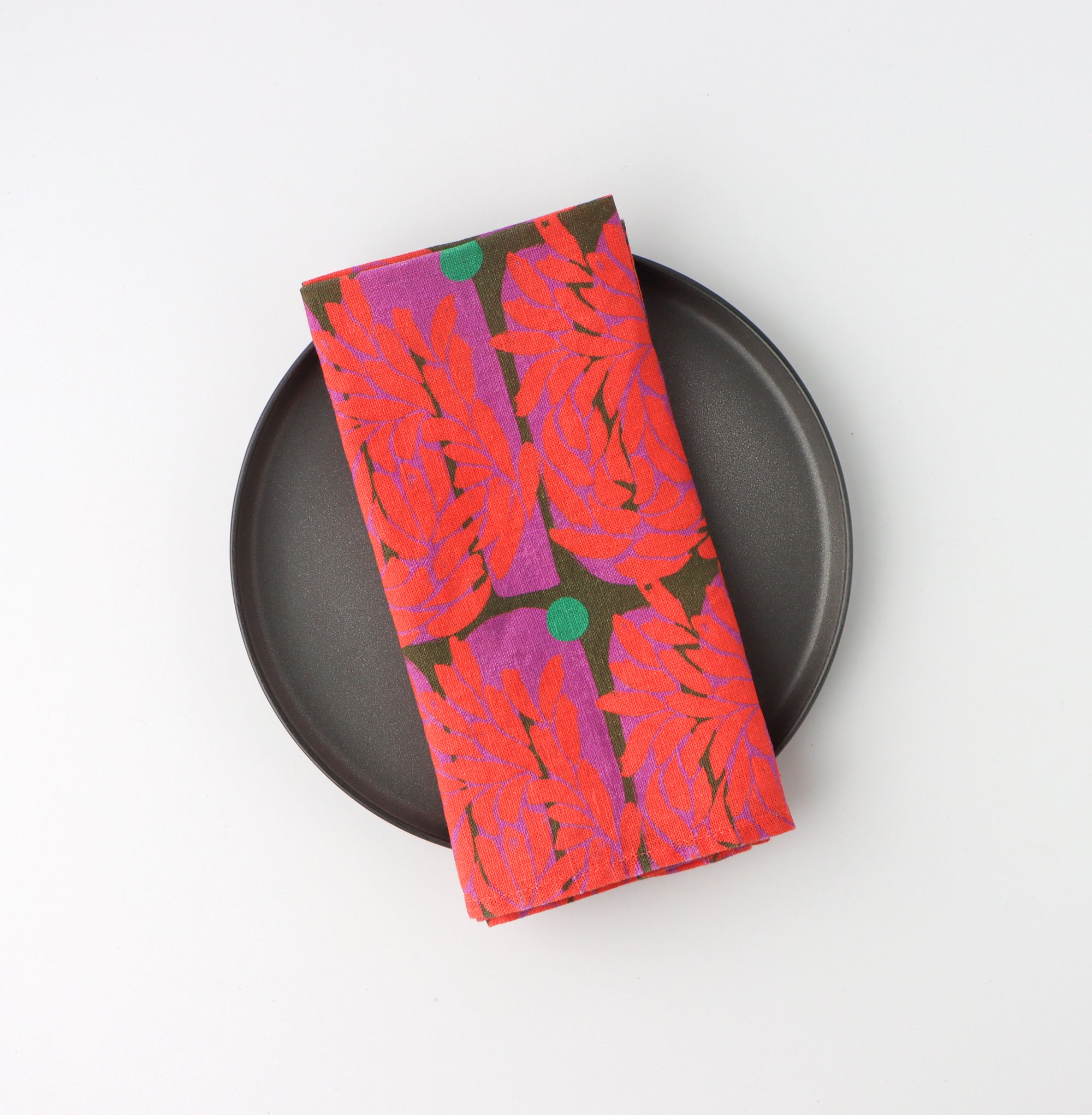 Red floral leaf-patterned napkin on a black plate against a white background. Designed by artist Leila Simon Hayes.