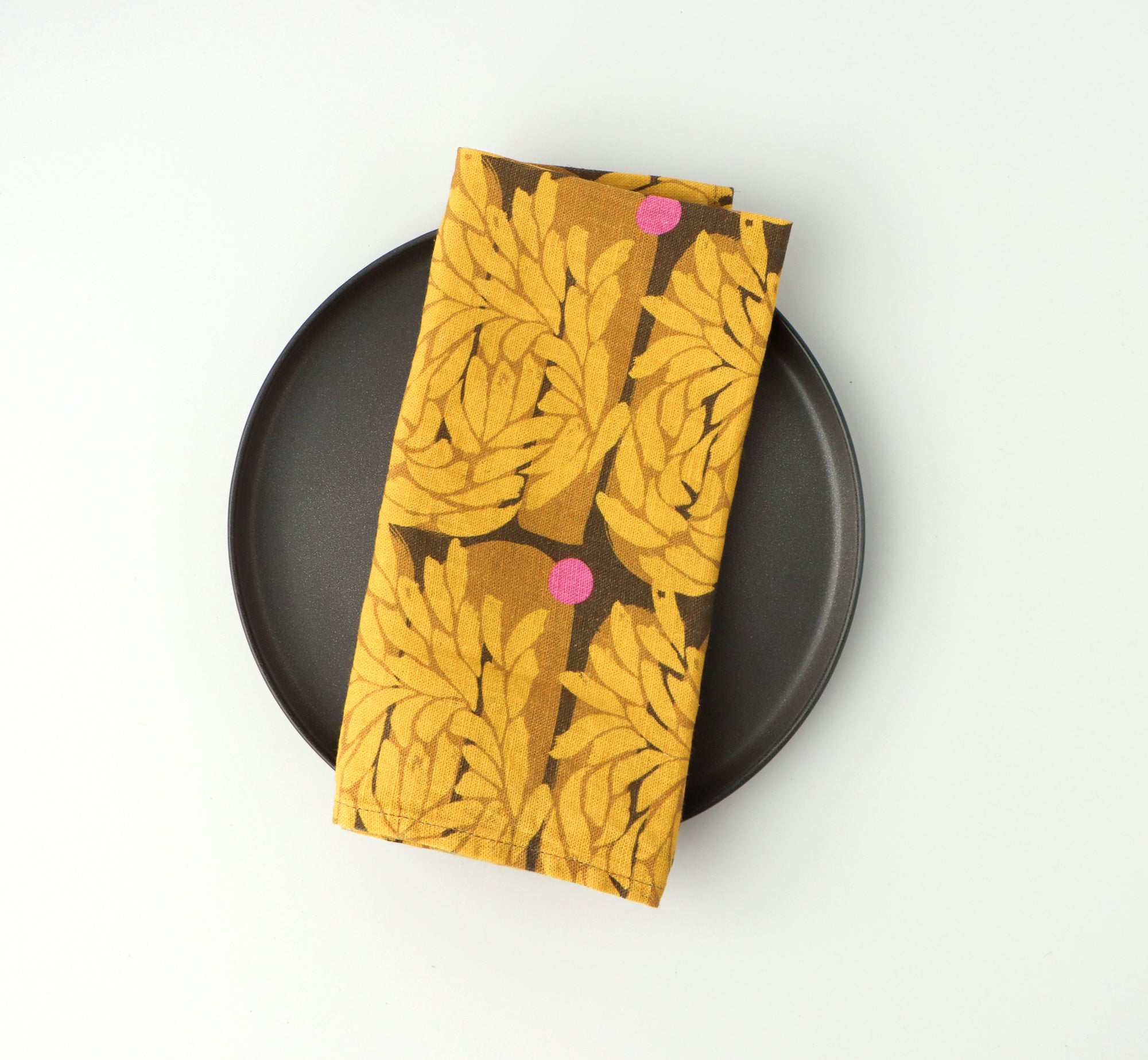 Napkin with yellow floral pattern on a black plate against a white background, designed by artist Leila Simon Hayes. 