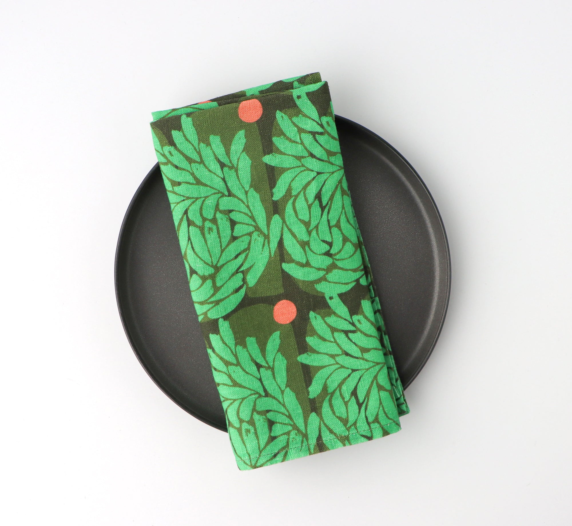 Green leaf-patterned napkin on a black plate against a white background. Designed by artist Leila Simon Hayes.