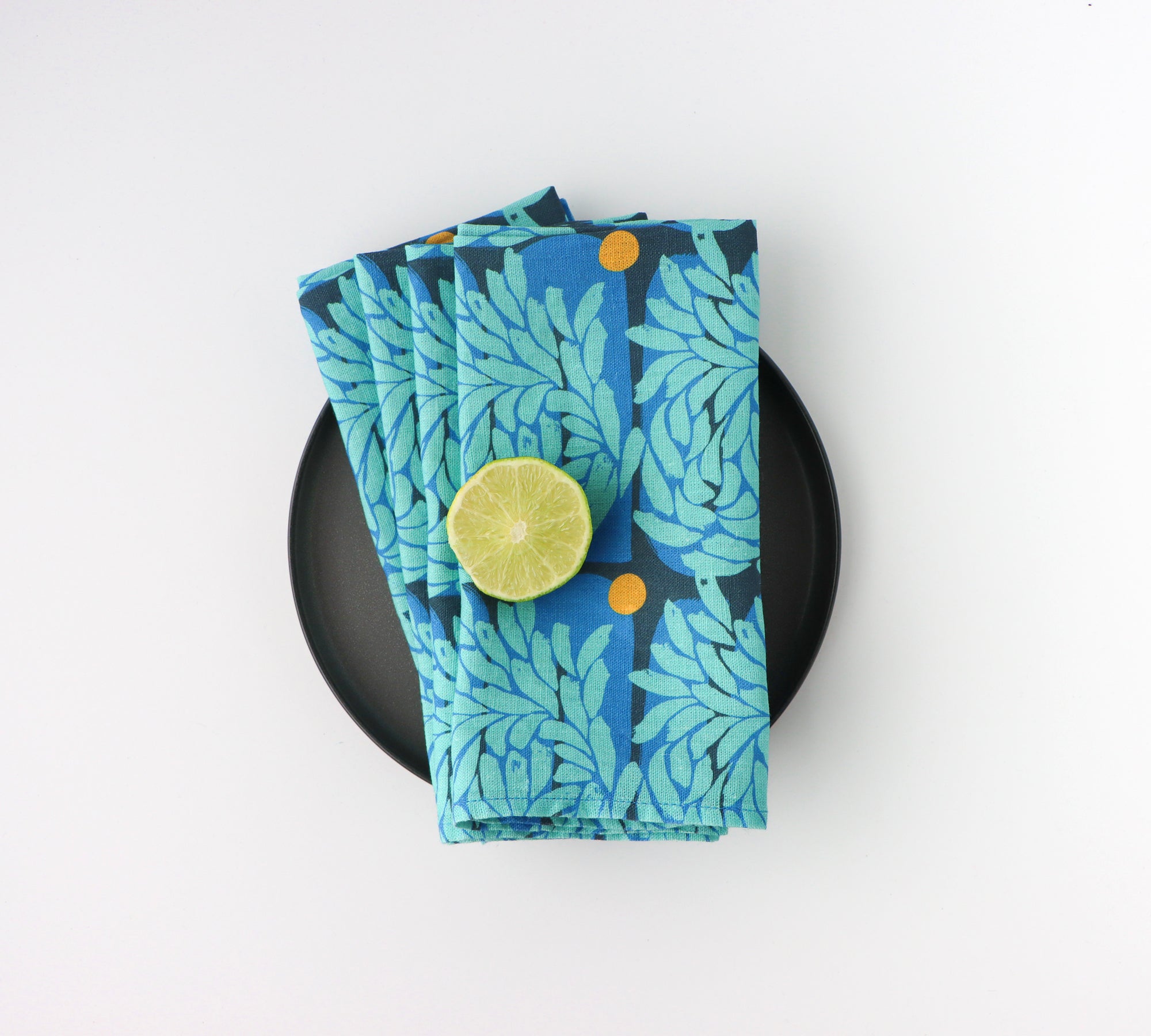 Set of four blue floral patterned napkins on a black plate with a white background. Designed by artist Leila Simon Hayes.