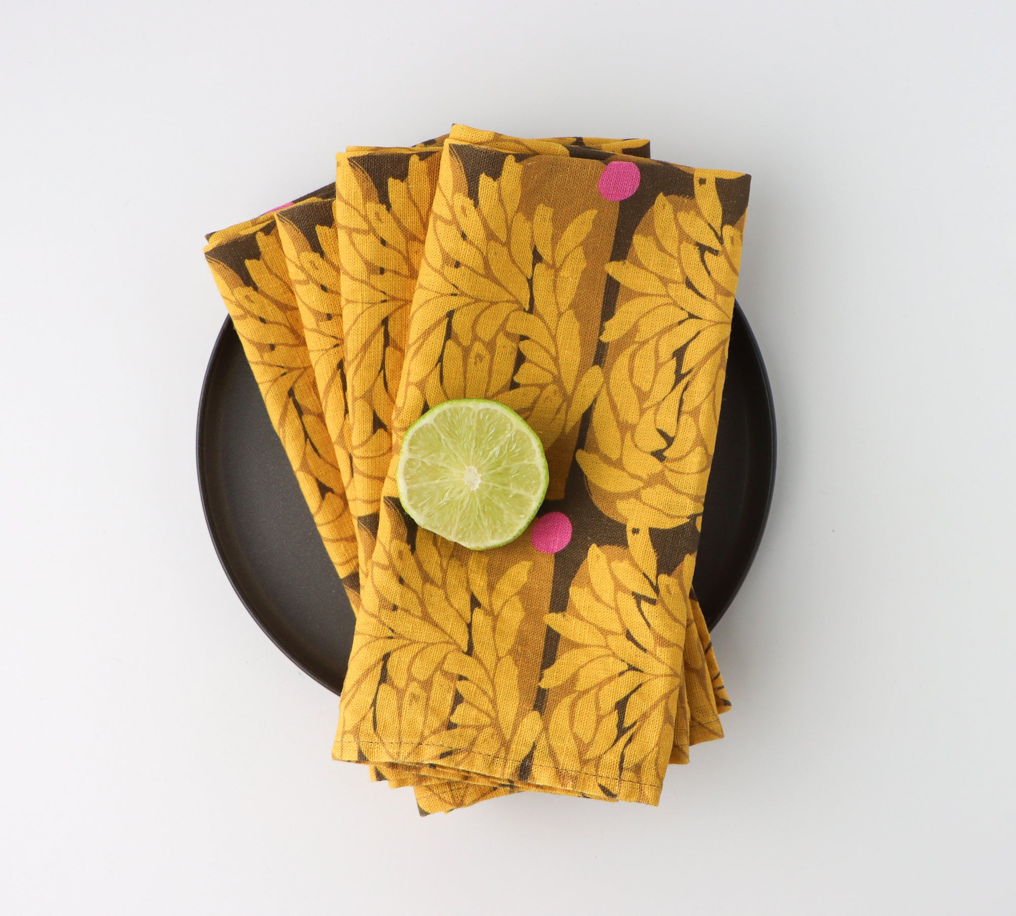 Four folded and layered dinner napkins with a vibrant yellow floral pattern, designed by artist Leila Simon Hayes.