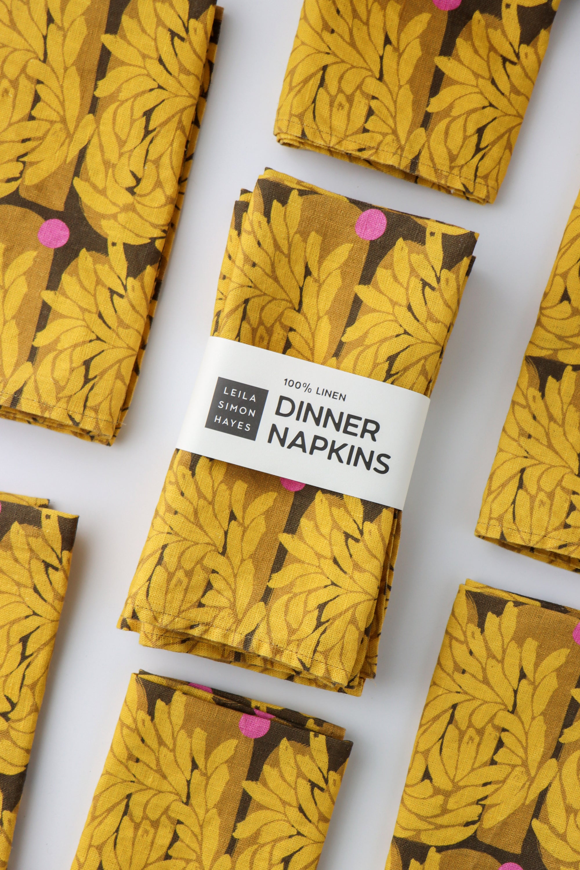 Pack of four packaged dinner napkins with a vibrant yellow floral pattern with a label saying "100% Linen Dinner Napkins", designed by artist Leila Simon Hayes.