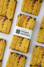 Pack of four packaged dinner napkins with a vibrant yellow floral pattern with a label saying "100% Linen Dinner Napkins", designed by artist Leila Simon Hayes.