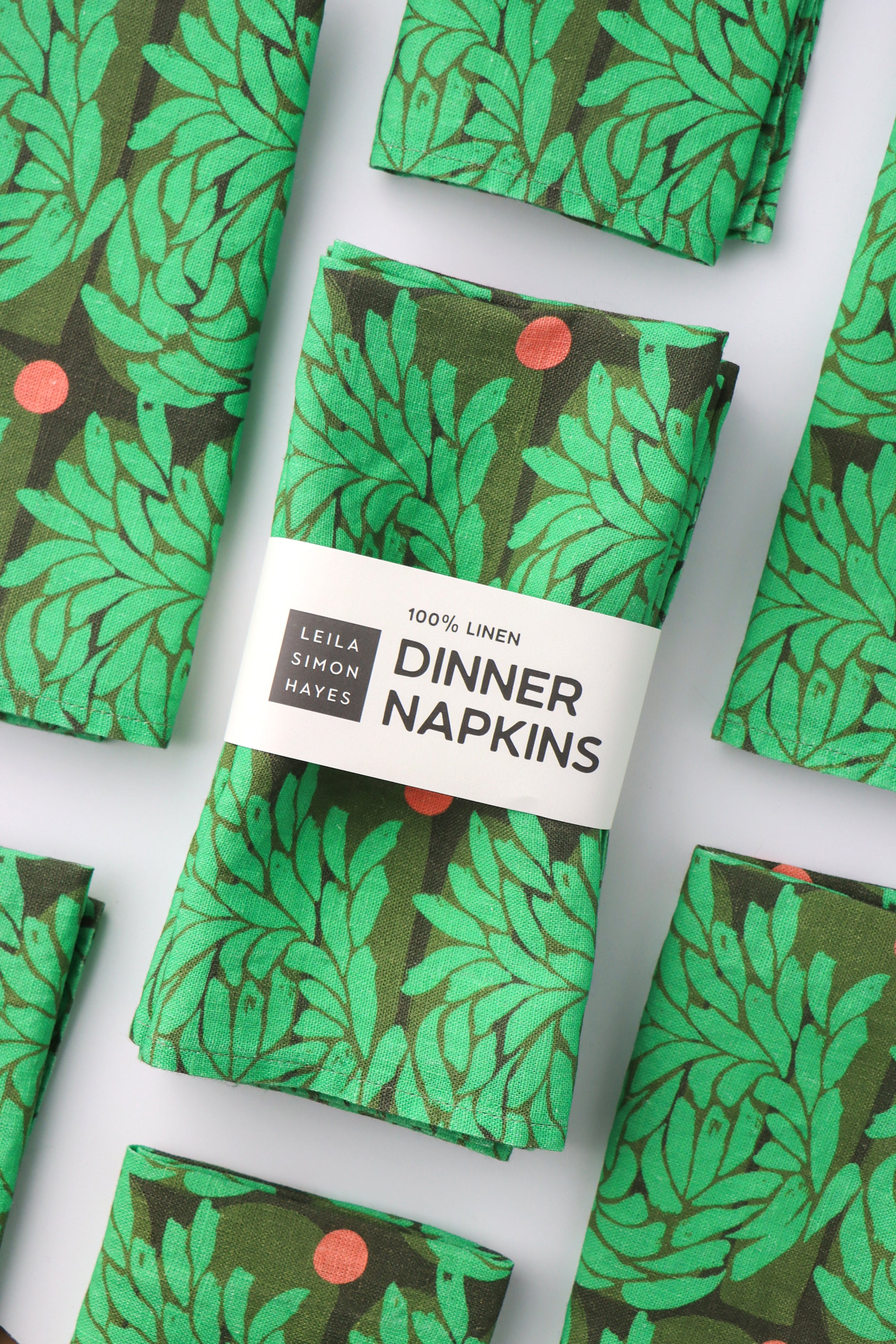 Pack of four, green floral leaf-patterned dinner napkins with a label saying "100% Linen Dinner Napkins", designed by artist Leila Simon Hayes.