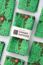 Pack of four, green floral leaf-patterned dinner napkins with a label saying "100% Linen Dinner Napkins", designed by artist Leila Simon Hayes.