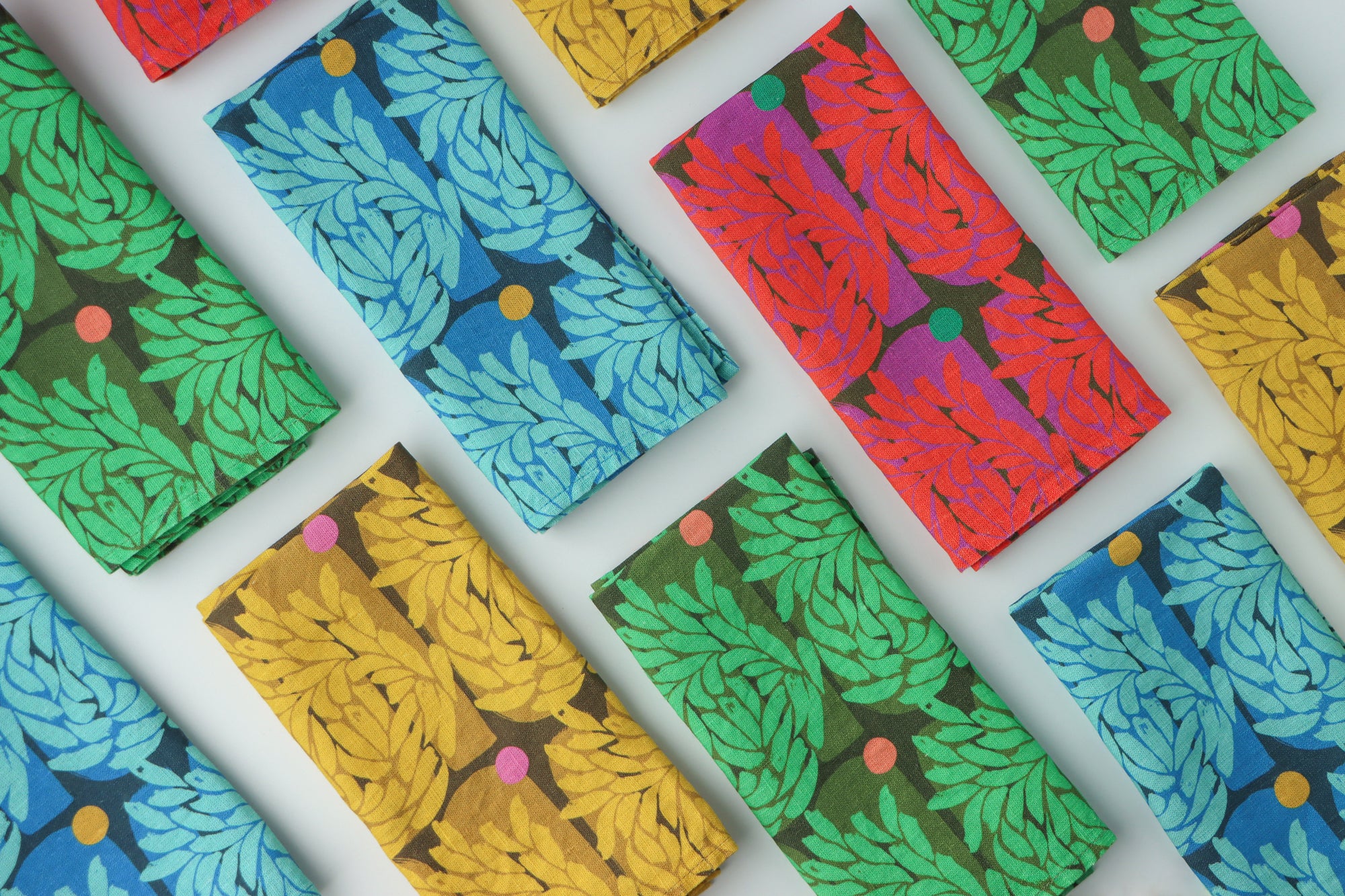 Colorful patterned napkins folded into a fourth and arranged in a grid on a white background. They are red, green, blue, and yellow. Designed by artist Leila Simon Hayes.