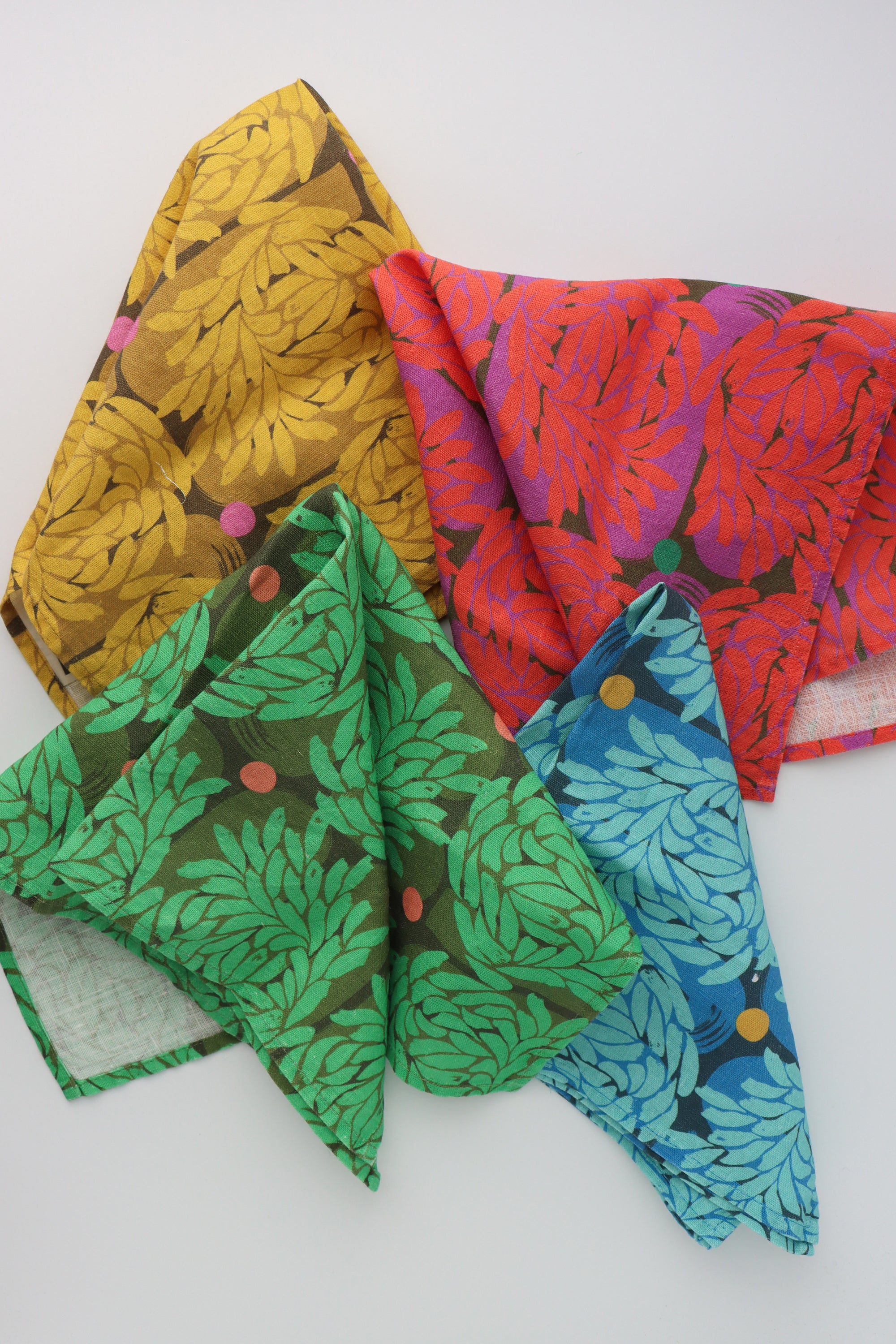 Four different colored napkins with the same abstract floral design by artist Leila Simon Hayes. The colors are yellow, red, green and blue and they are spread across a white background.