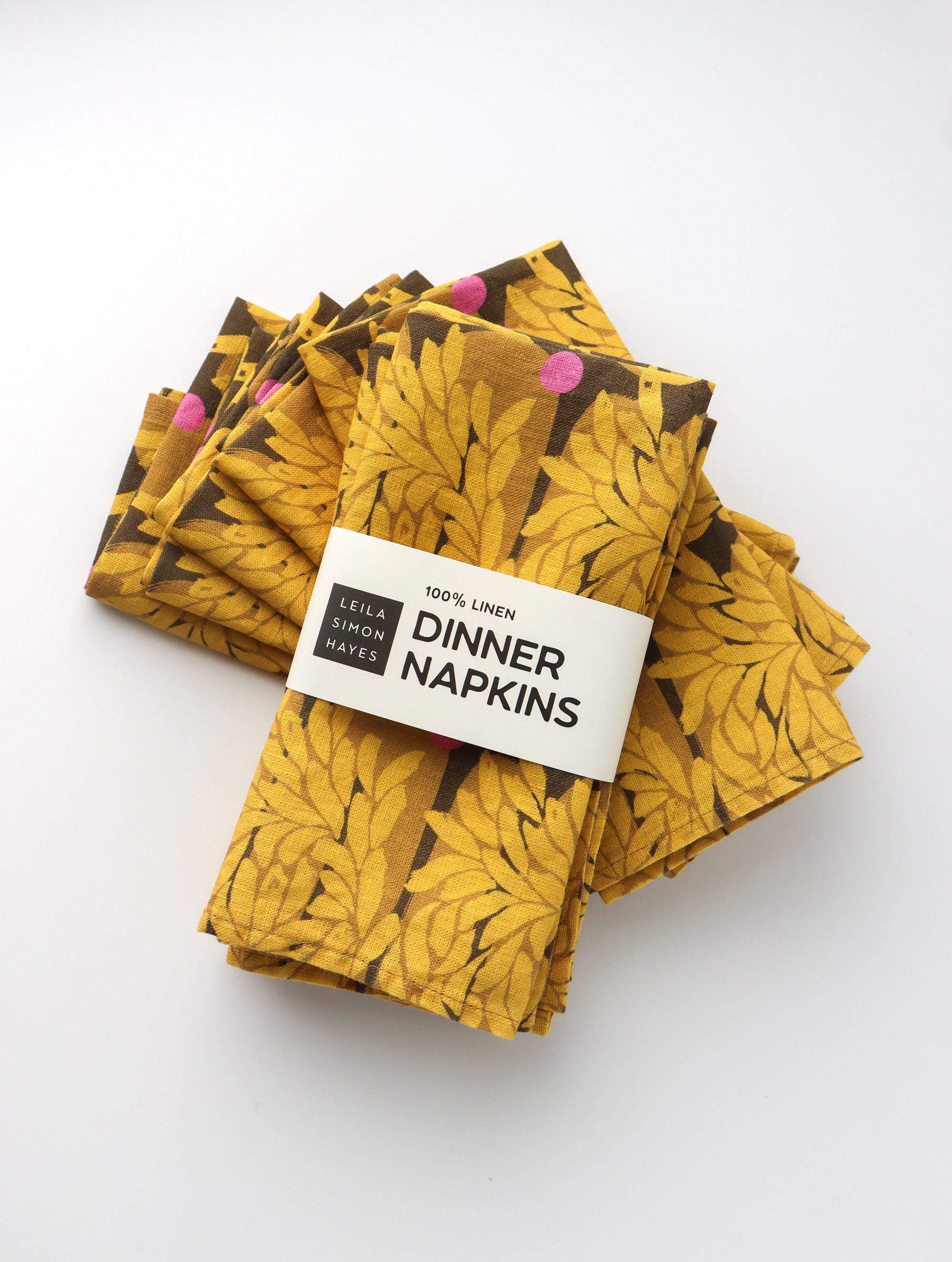 Pack of four packaged dinner napkins with a vibrant yellow floral pattern with a label saying "100% Linen Dinner Napkins", designed by artist Leila Simon Hayes.