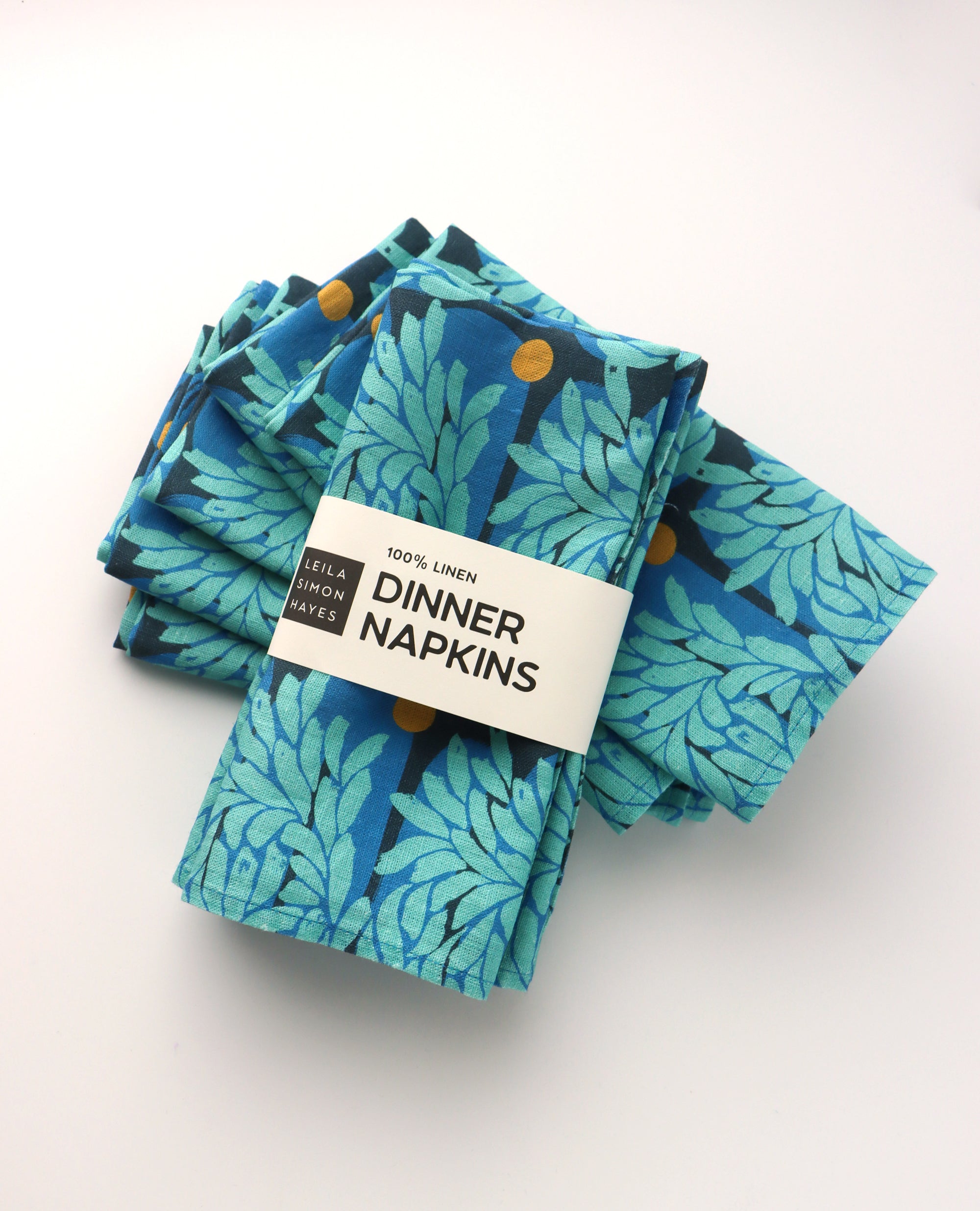 Set of four blue floral leaf-patterned dinner napkins with a label saying "100% Linen Dinner Napkins", designed by artist Leila Simon Hayes.