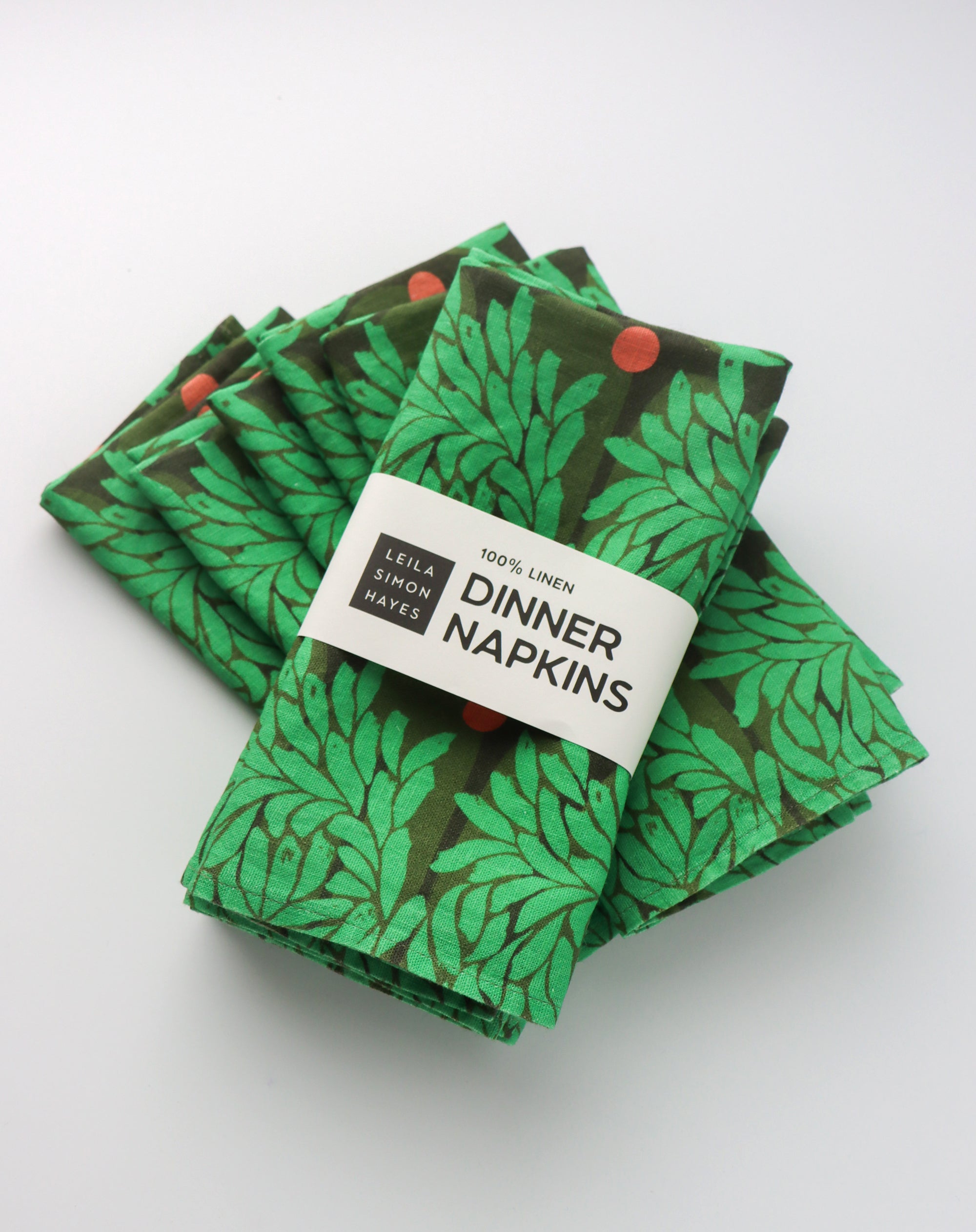 Pack of four, green floral leaf-patterned dinner napkins with a label saying "100% Linen Dinner Napkins", designed by artist Leila Simon Hayes.