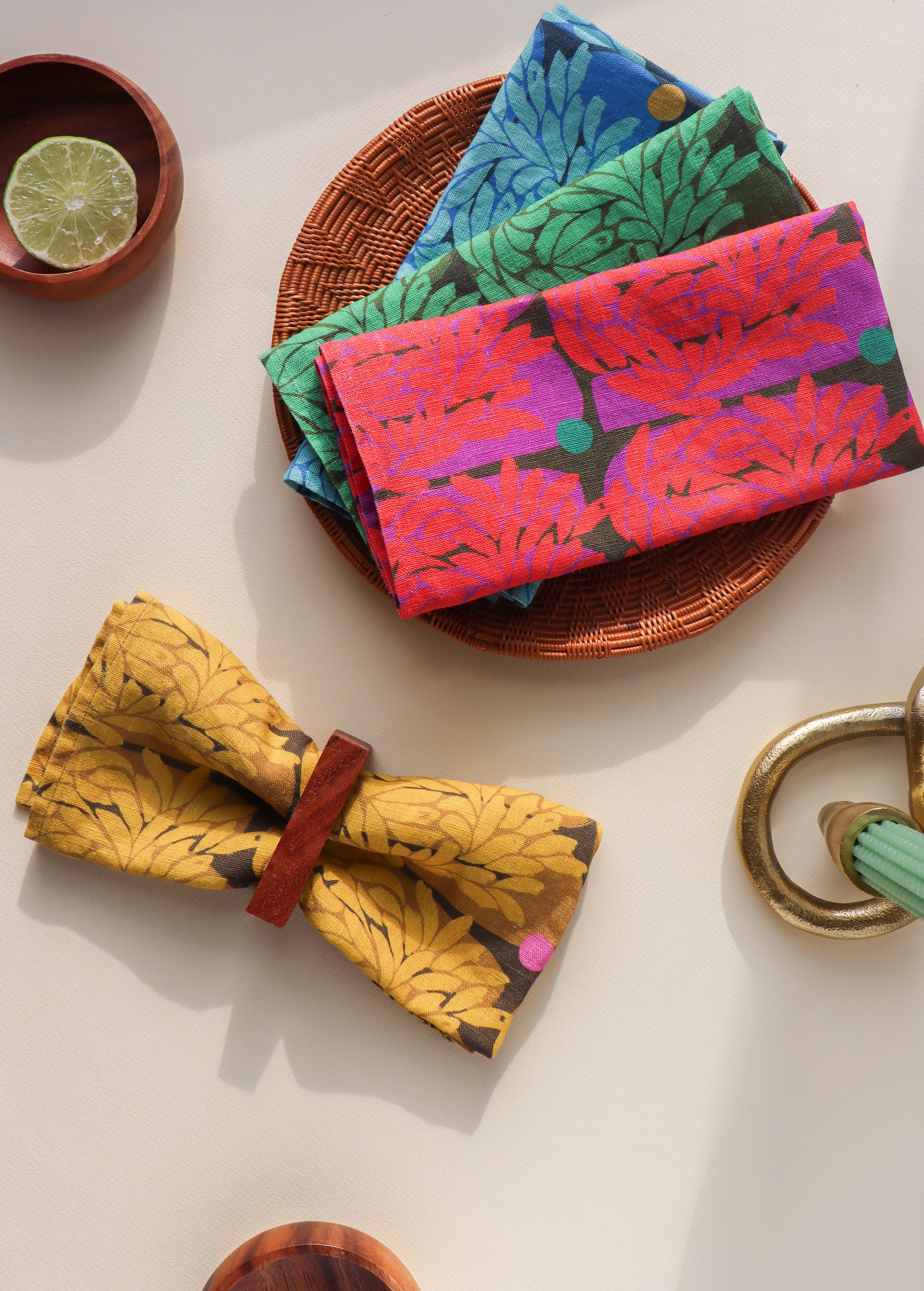 Four colorful and floral patterned napkins on a white surface with a bowl and lime. The napkins are folded and designed by artist Leila Simon Hayes.