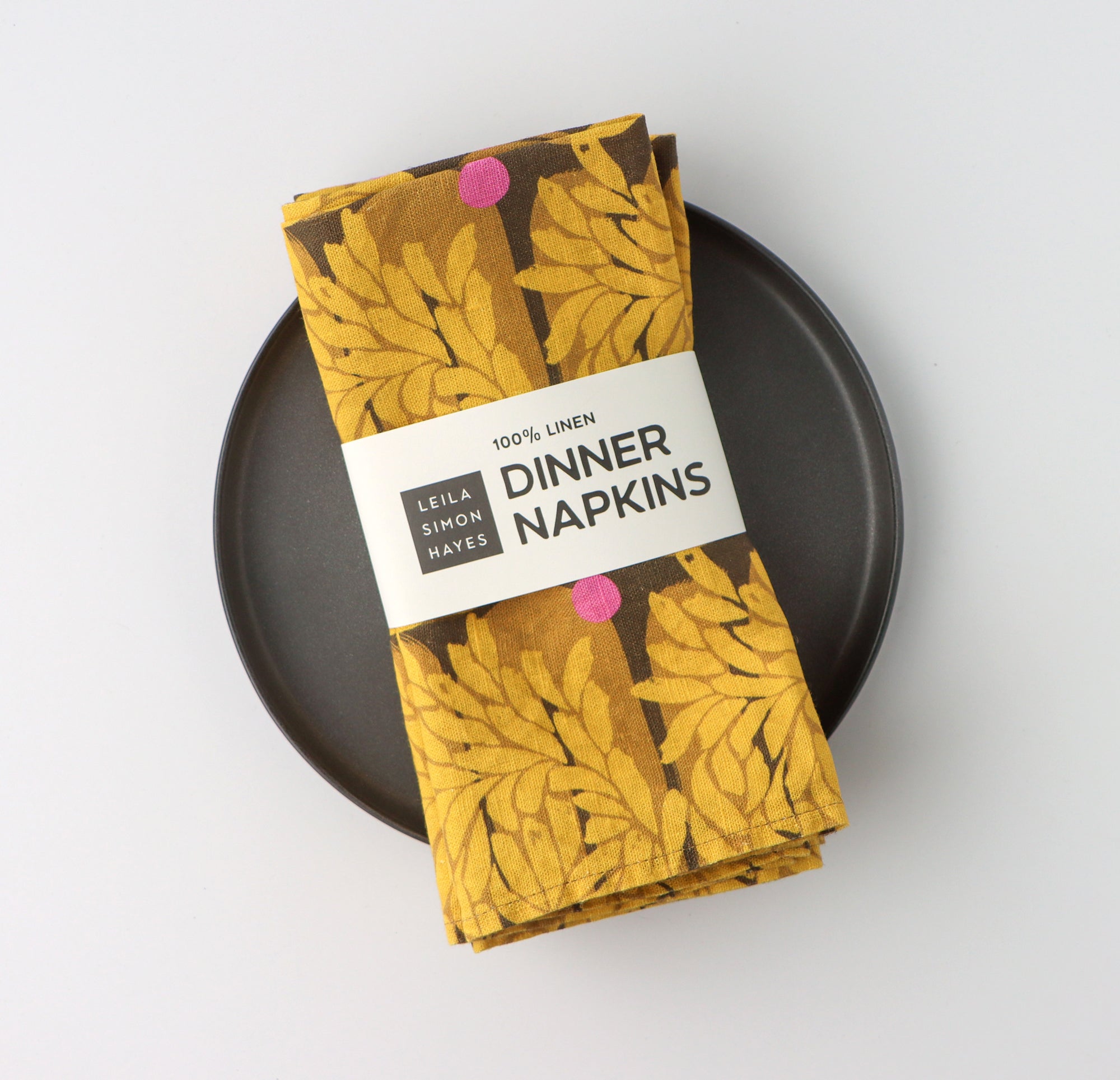 Pack of four packaged dinner napkins with a vibrant yellow floral pattern with a label saying "100% Linen Dinner Napkins", designed by artist Leila Simon Hayes.
