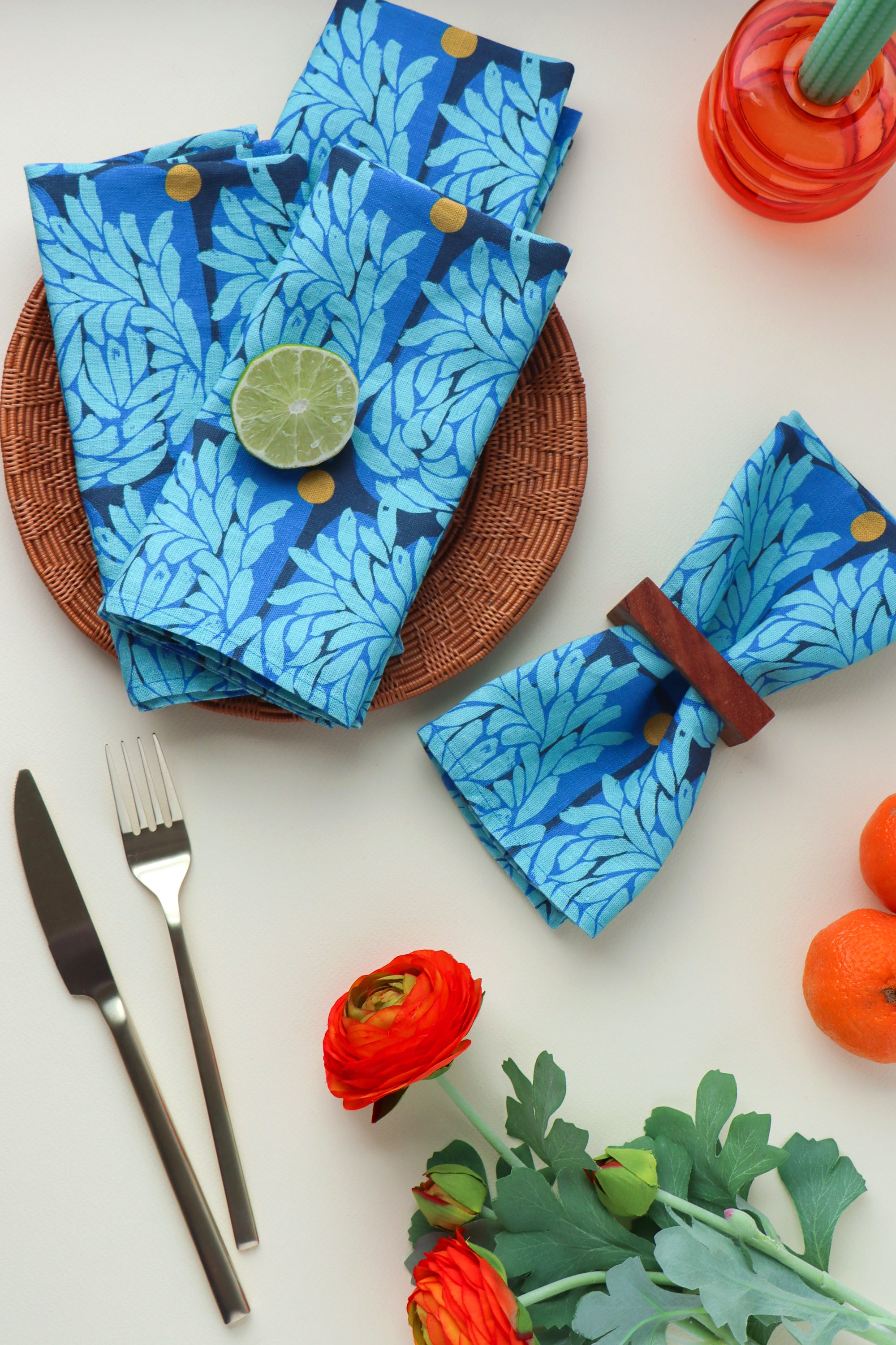 Four blue floral-patterned napkins on a white table with cutlery and flowers. Designed by artist Leila Simon Hayes.