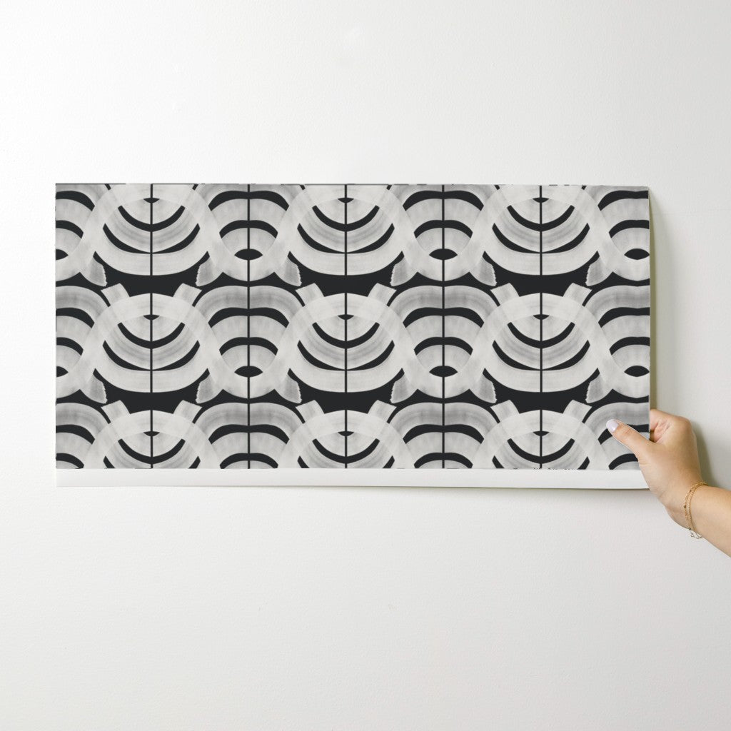 Hand holding a rectangular tile with a black and white geometric pattern on a light gray background. Designed by artist Leila Simon Hayes.