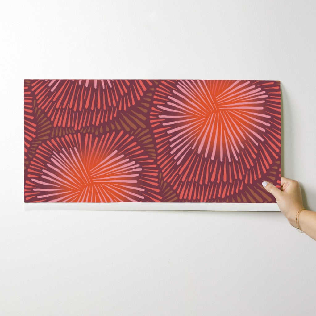 Hand holding a wallpaper swatch with a red and purple abstract pattern against a white background. Designed by artist Leila Simon Hayes.