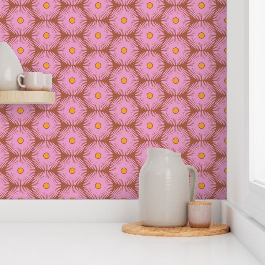 A section of wallpaper with a pink background and a geometric pattern of overlapping flower shapes in a brownish-pink color, with a vase and other home decor items in the background. Designed by artist Leila Simon Hayes.