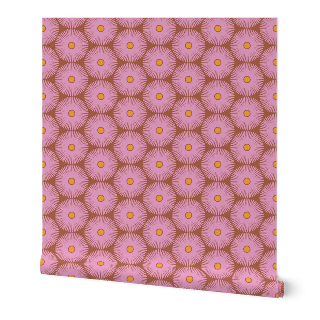 A roll of wallpaper featuring a repeating pattern of pink flowers with yellow centers on a brown background. Designed by artist Leila Simon Hayes.