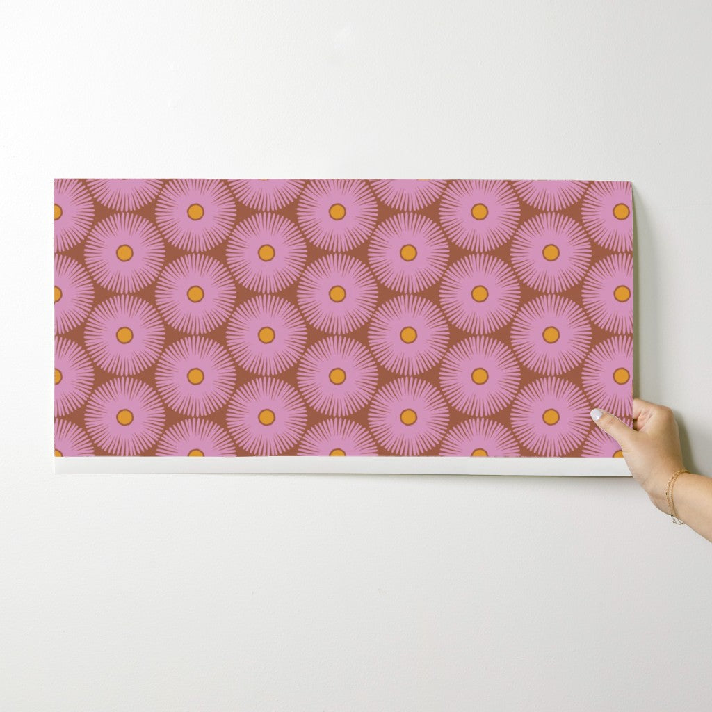 Hand holding a pink and brown patterned wallpaper swatch on a white surface. Designed by artist Leila Simon Hayes.