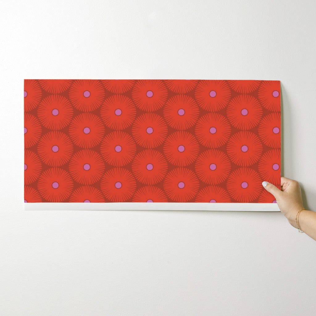 Hand holding a red wallpaper swatch against a white background. Designed by artist Leila Simon Hayes.