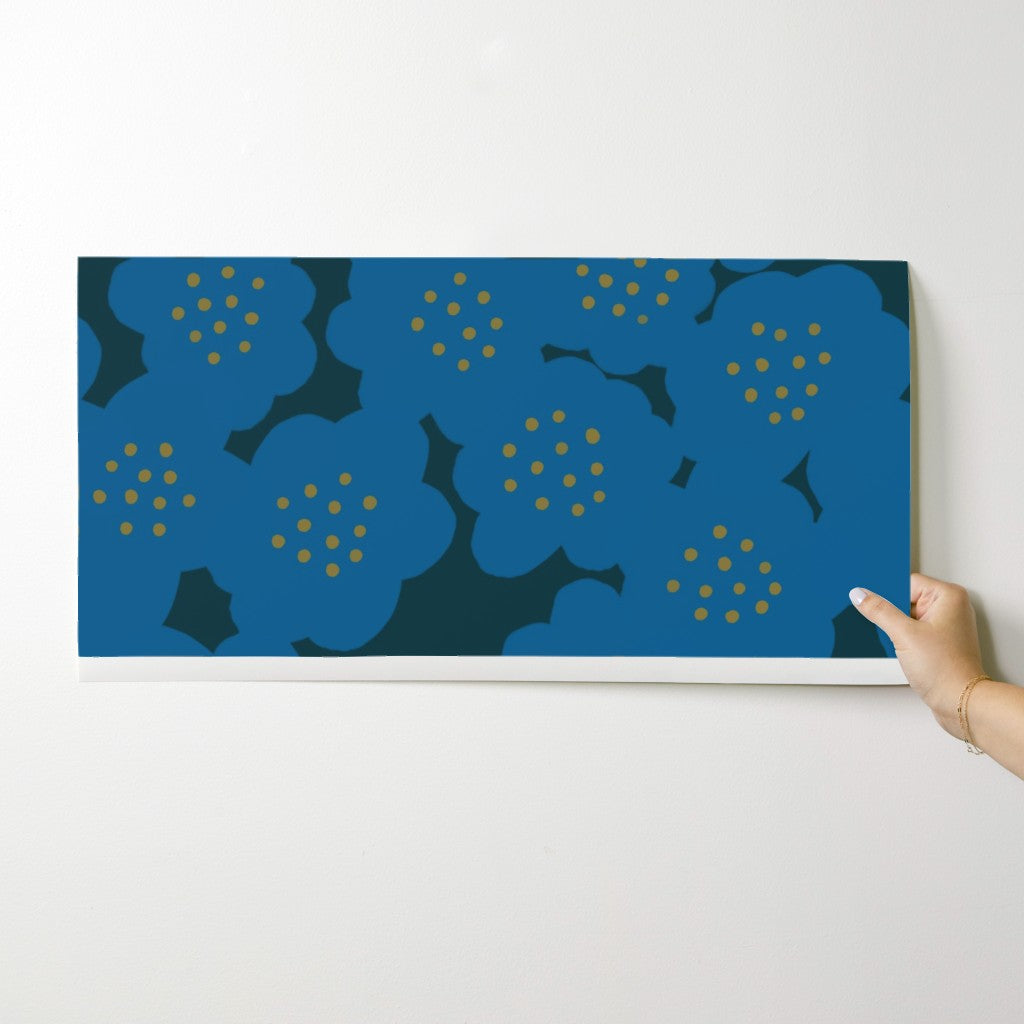 Hand holding a blue floral wallpaper swatch against a white wall. Designed by artist Leila Simon Hayes.