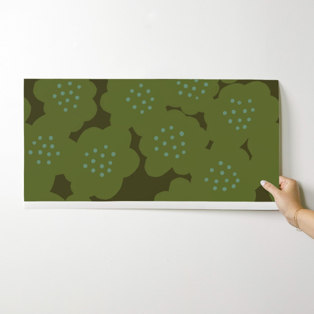Hand holding a green floral patterned wallpaper swatch against a white wall. Designed by artist Leila Simon Hayes.
