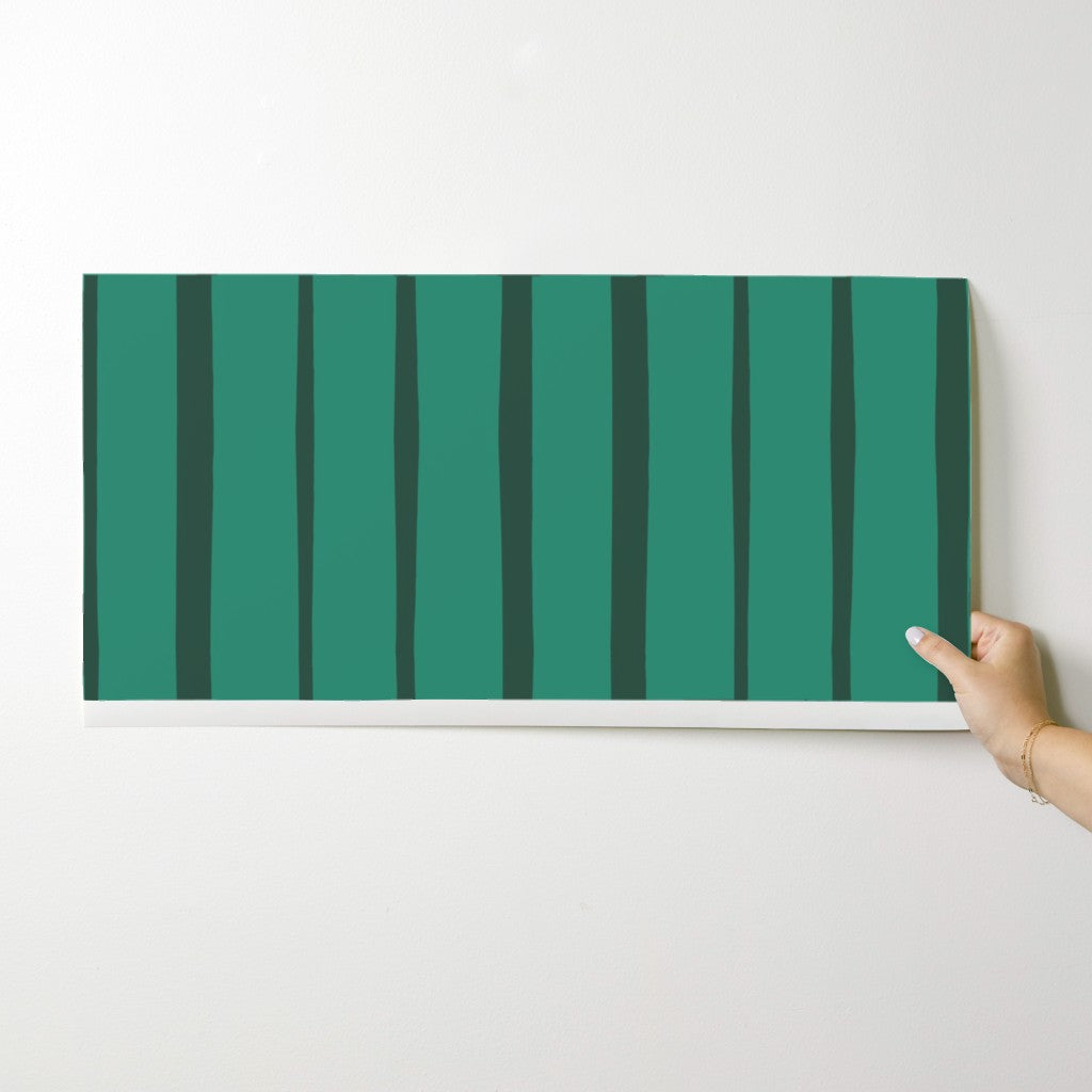 Hand holding a green striped wallpaper swatch against a white background. Designed by artist Leila Simon Hayes.