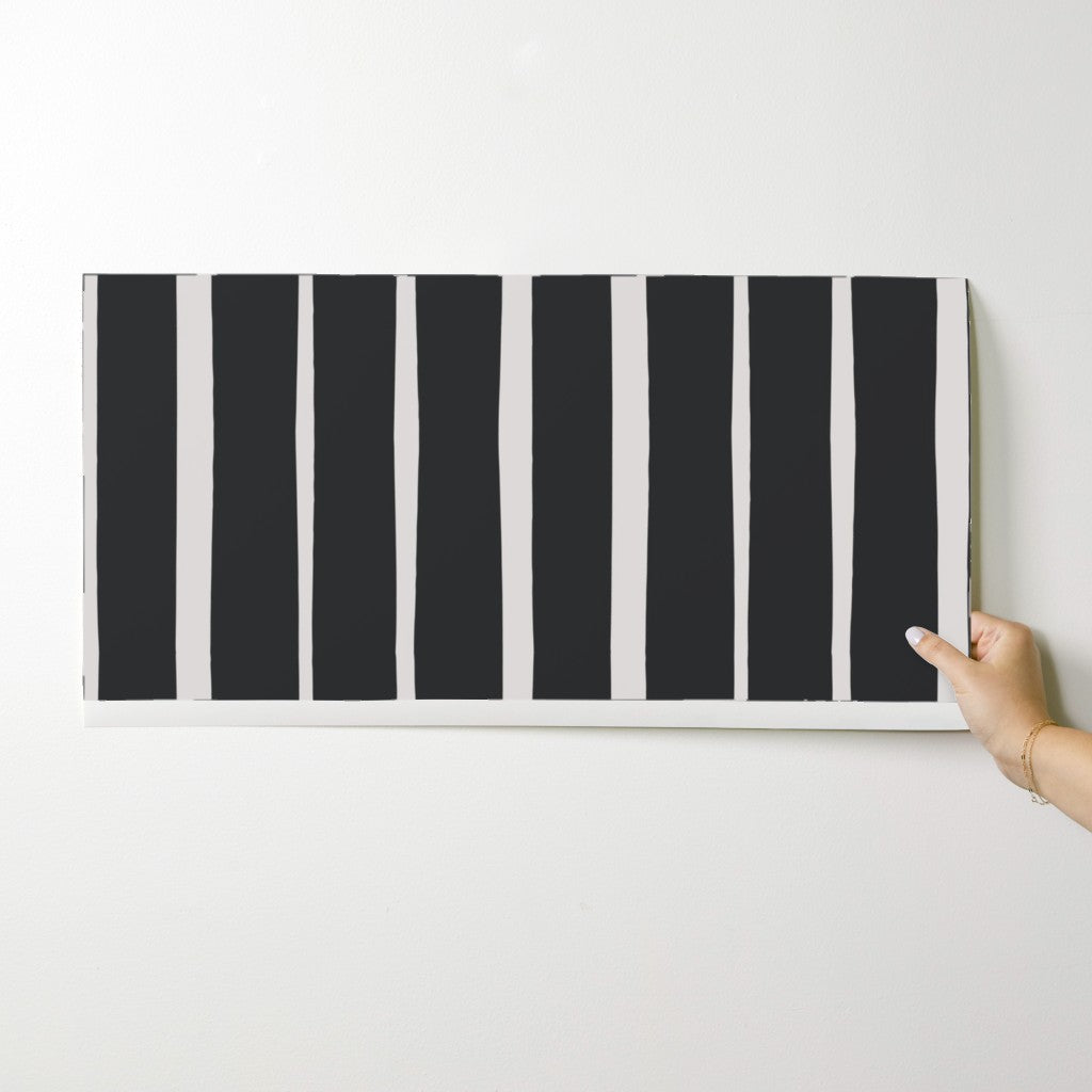 Black and white striped wallpaper swatch held by a hand on a light gray background. Designed by artist Leila Simon Hayes.