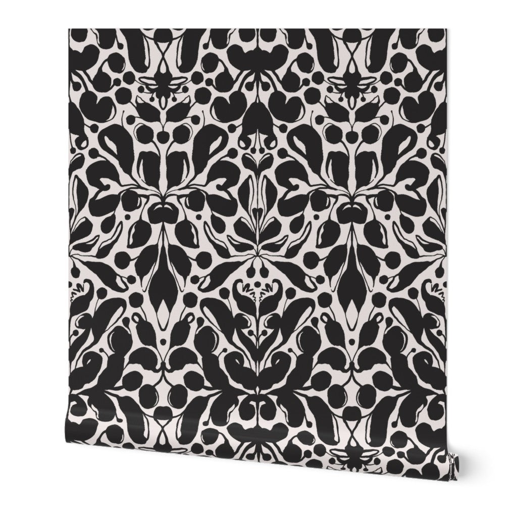 Roll of peel-and-stick wallpaper on a white background. The wallpaper is a black kaleidoscope, botanical, and floral pattern on a white base. Designed by artist Leila Simon Hayes.