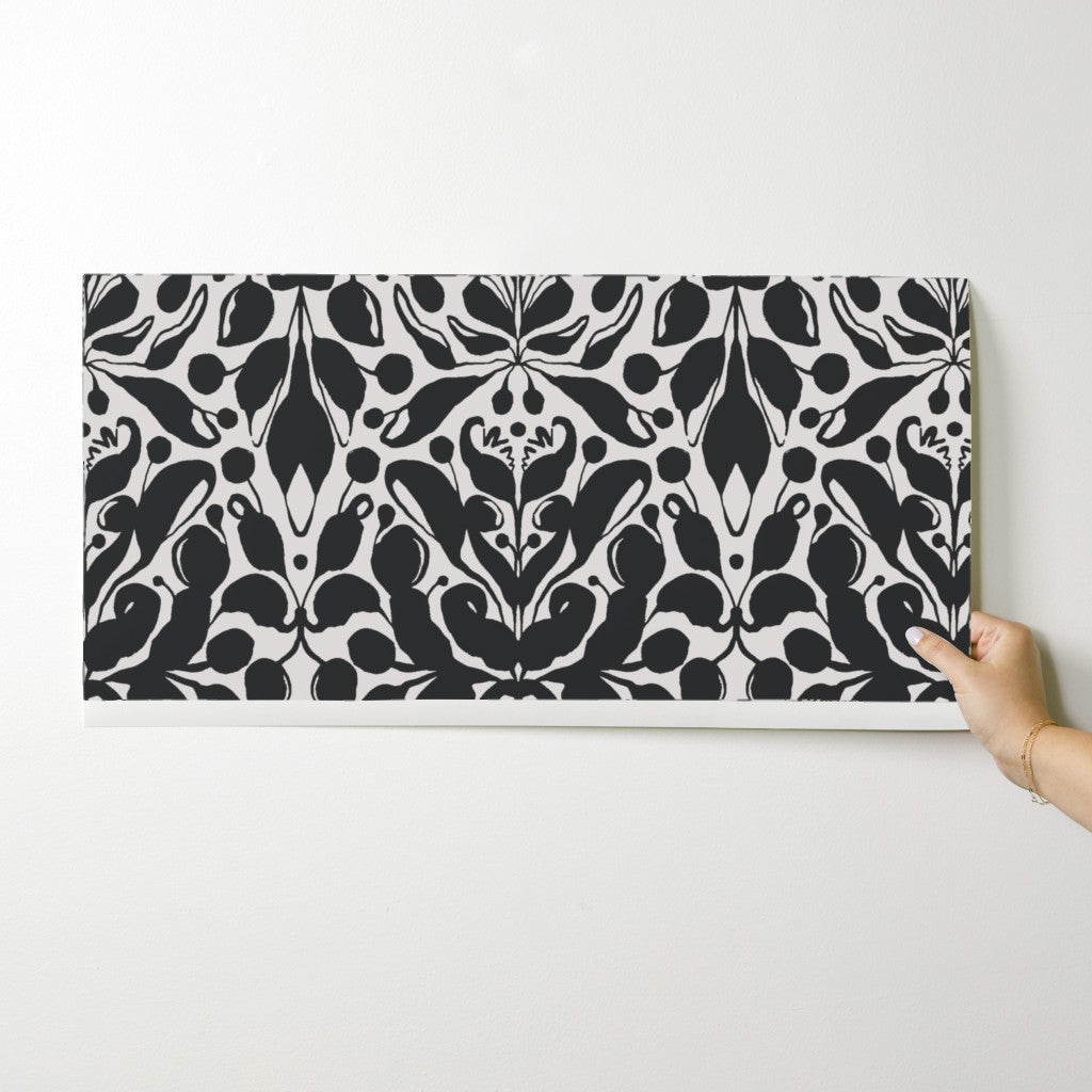 Person holding a black and white patterned wallpaper swatch against a white background. Designed by artist Leila Simon Hayes.