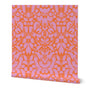 Roll of peel-and-stick wallpaper on a white background. The wallpaper is a light pink kaleidoscope, botanical, and floral pattern on an orange base. Designed by artist Leila Simon Hayes.