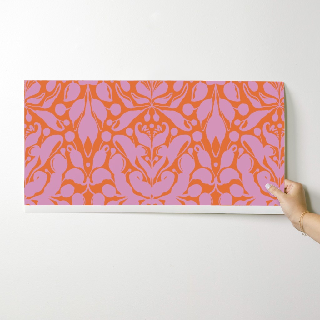 Hand holding a pink and orange patterned wallpaper swatch against a white background. Designed by artist Leila Simon Hayes.