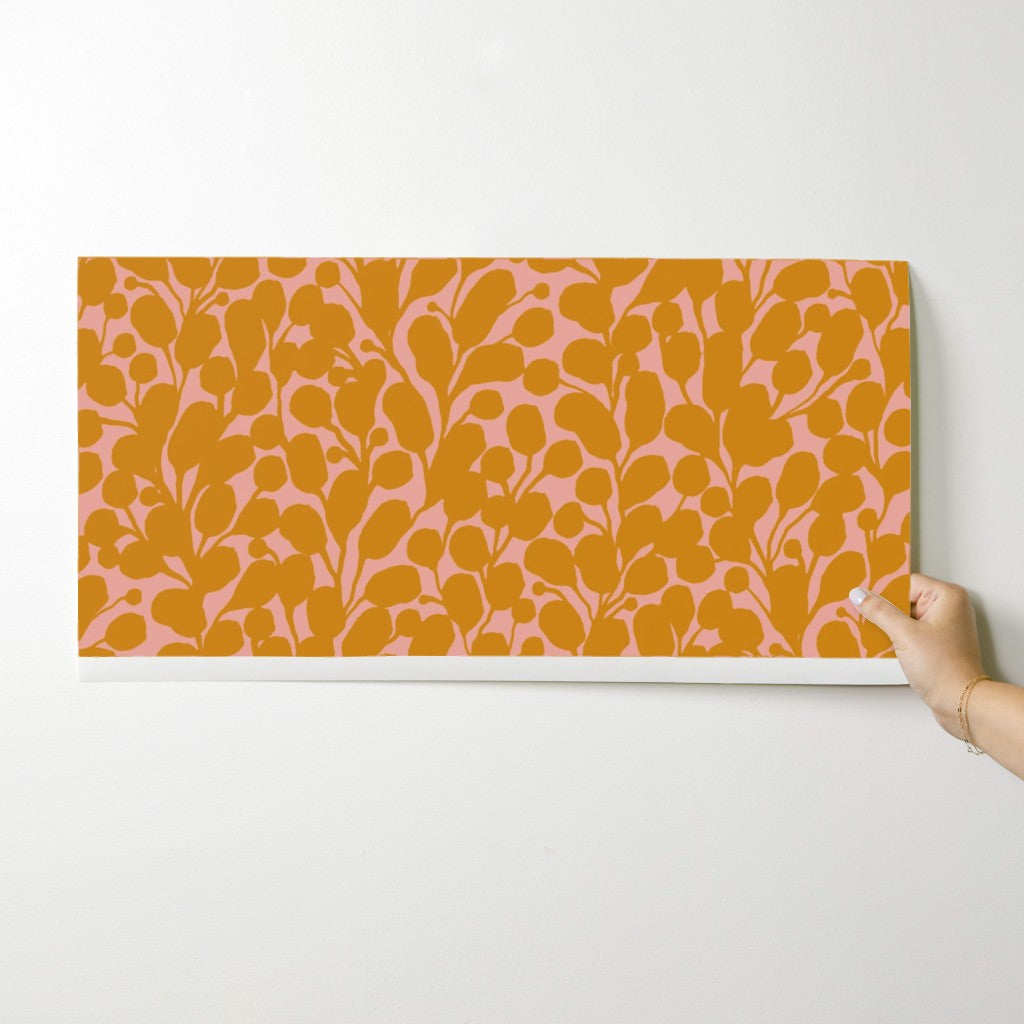 Hand holding a rectangular wallpaper swatch with a floral pattern on a white background. Designed by artist Leila Simon Hayes.