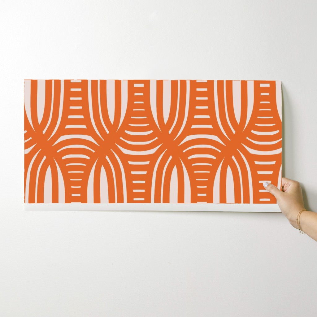 Hand holding a wallpaper swatch with an coral and white geometric pattern against a white background. Designed by artist Leila Simon Hayes.