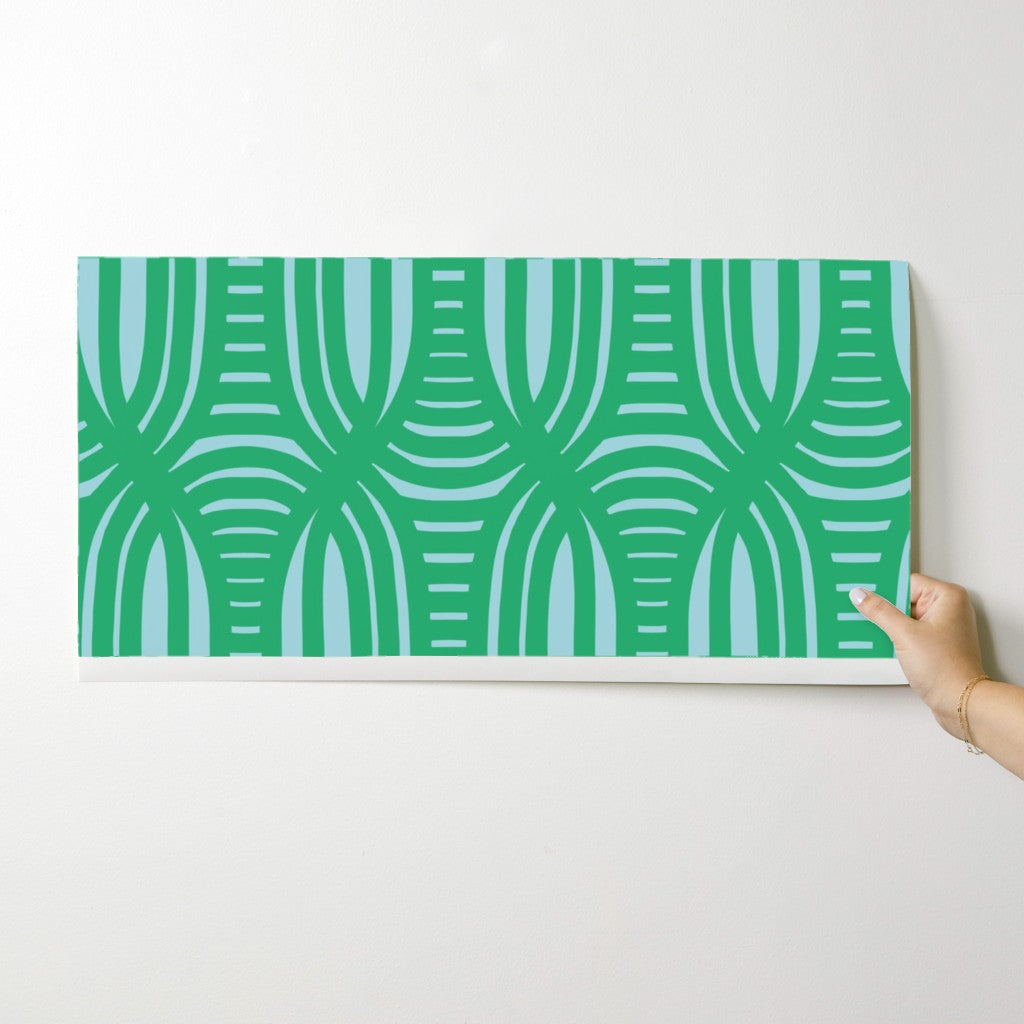Hand holding a green and blue patterned wallpaper swatch against a white background. Designed by artist Leila Simon Hayes.