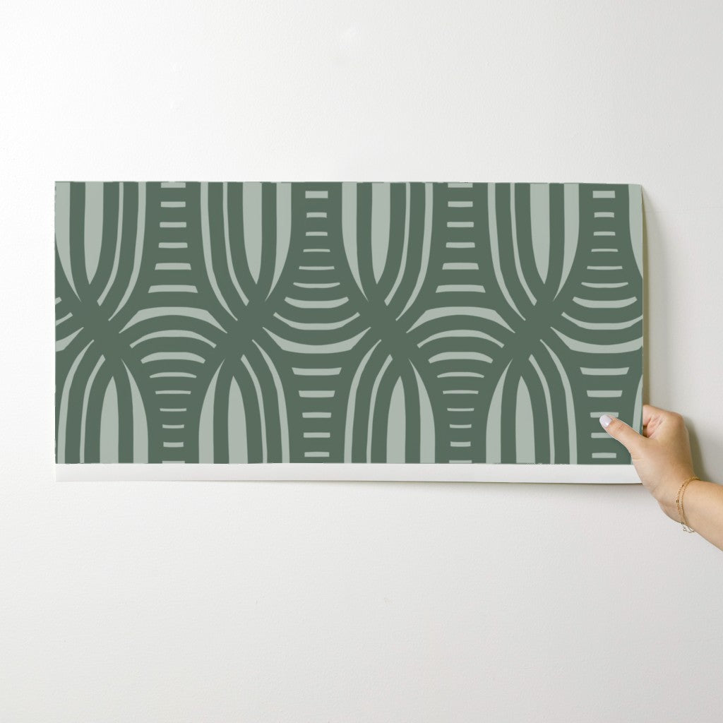 Hand holding a green patterned wallpaper swatch against a white background. Designed by artist Leila Simon Hayes.