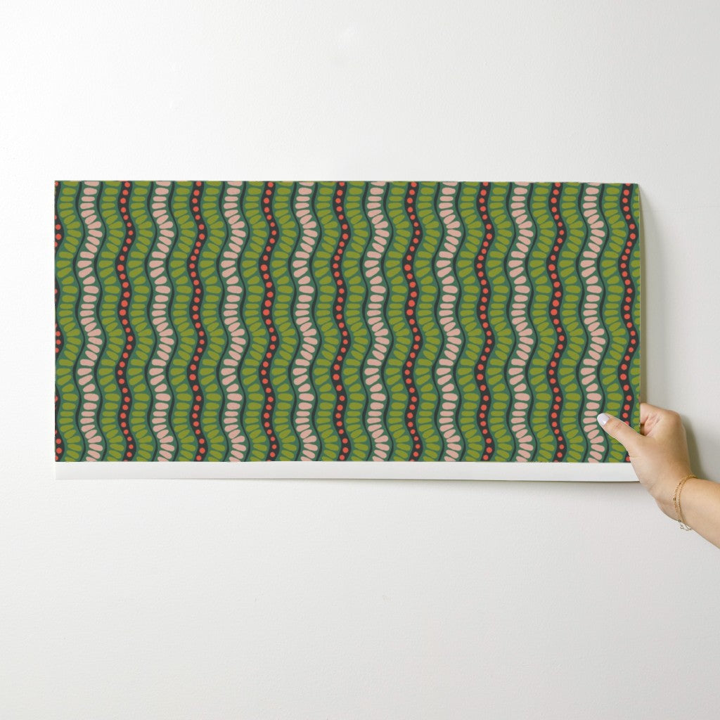 Hand holding a wallpaper swatch with a green and pink wavy pattern on a white background. Designed by artist Leila Simon Hayes. 