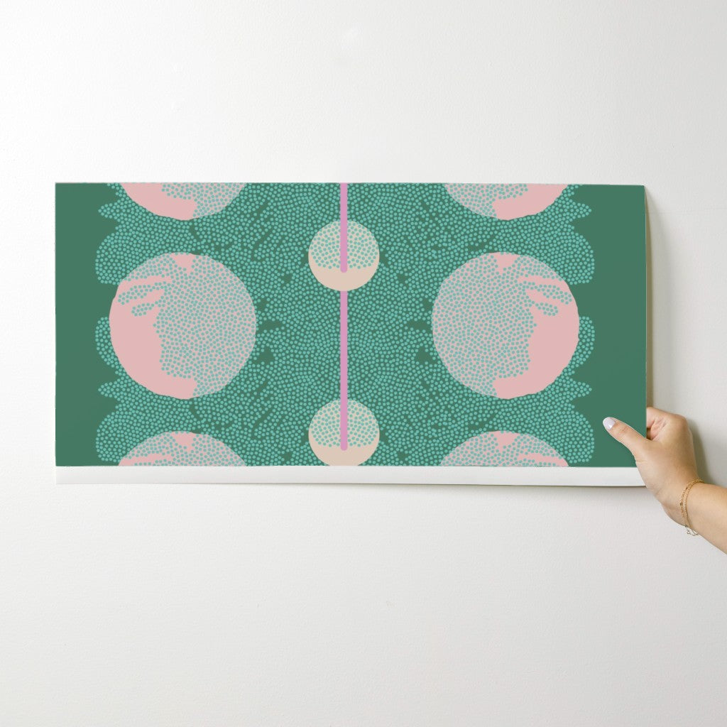 Hand holding a wallpaper swatch with a green and pink abstract pattern on a white surface. Designed by artist Leila Simon Hayes.