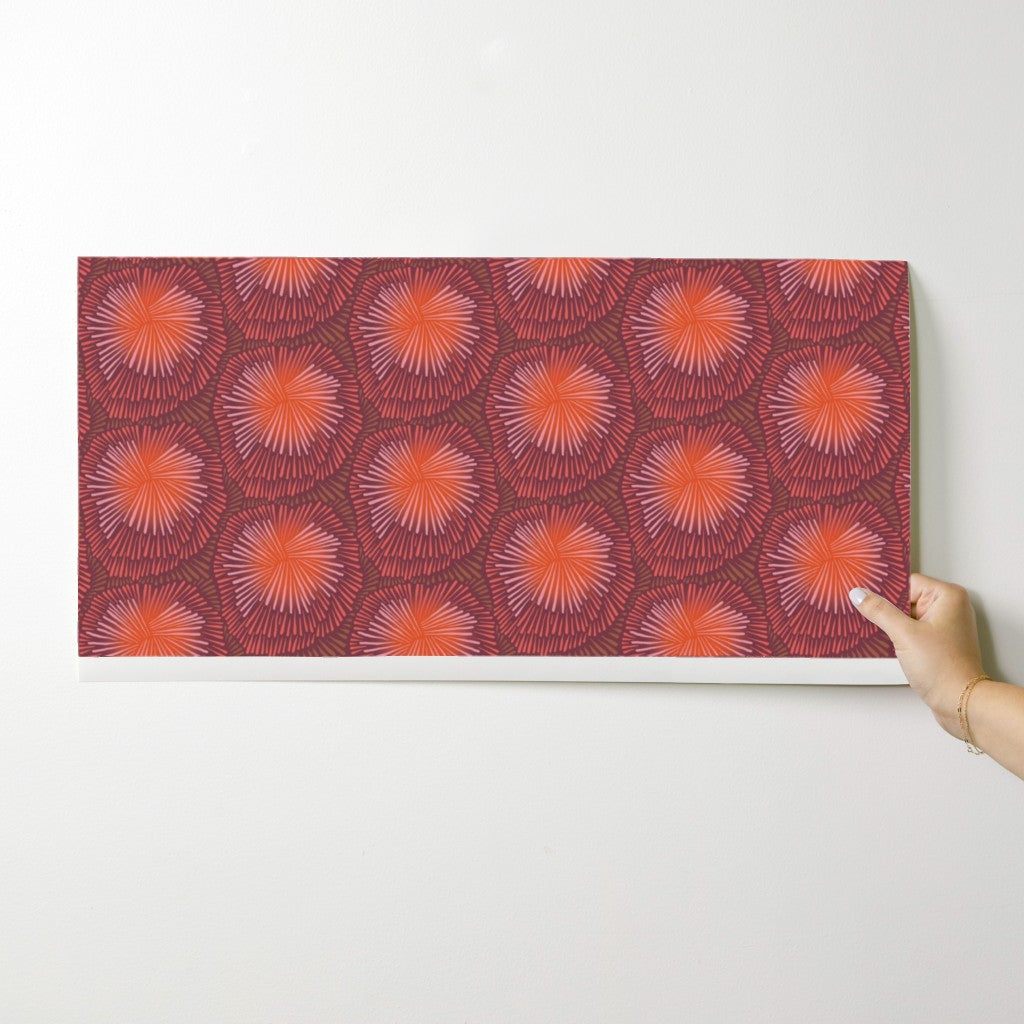 Hand holding a rectangular panel with a red and orange pattern against a white background. Designed by artist Leila Simon Hayes.